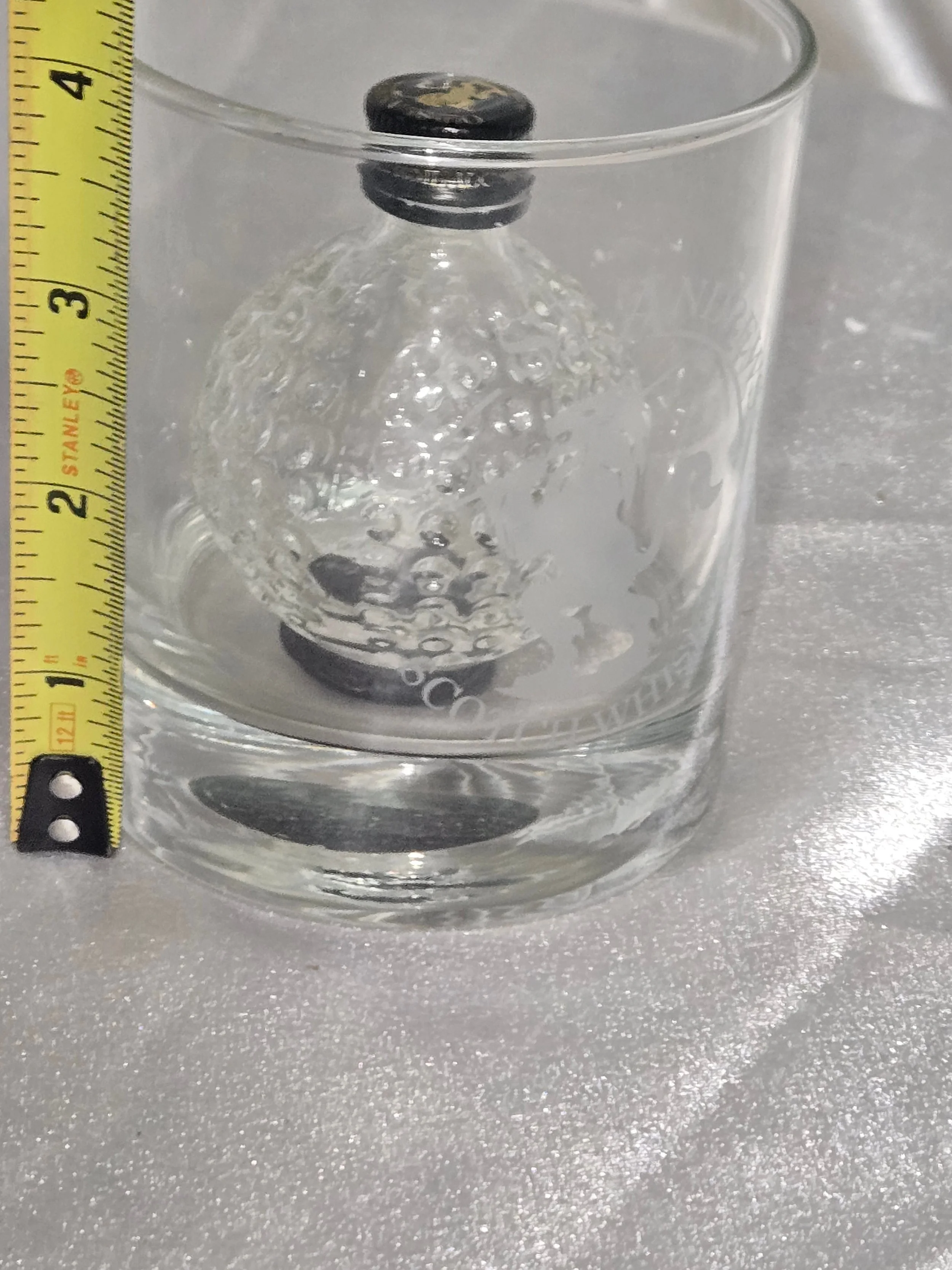 Side angle showing embossed golf ball texture of bottle inside rocks glass out of packaging showing measurements