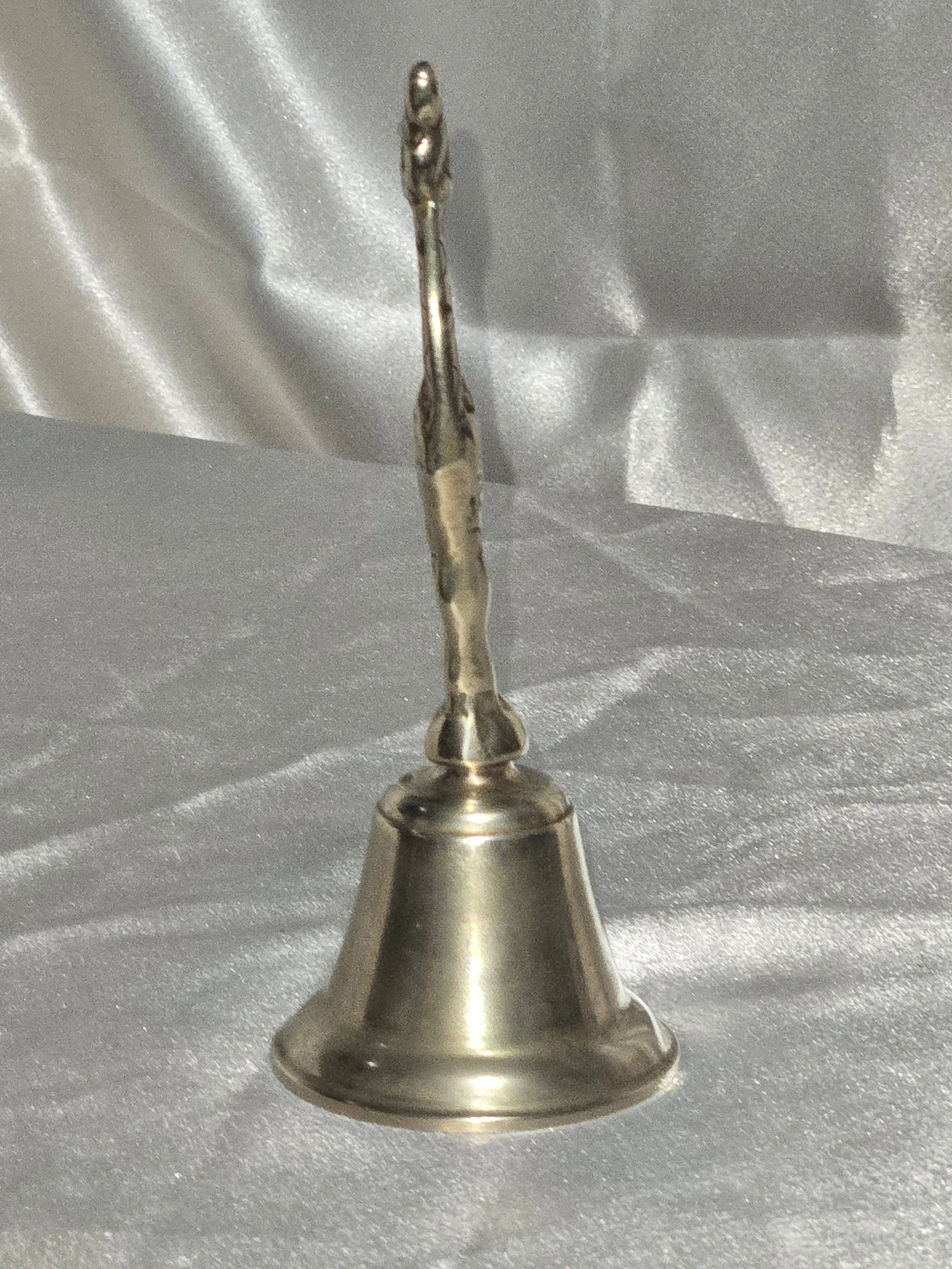 Close-up of vintage brass giraffe-shaped bell standing on silver background, 6 in tall mid-century safari collectible. Front facing side view