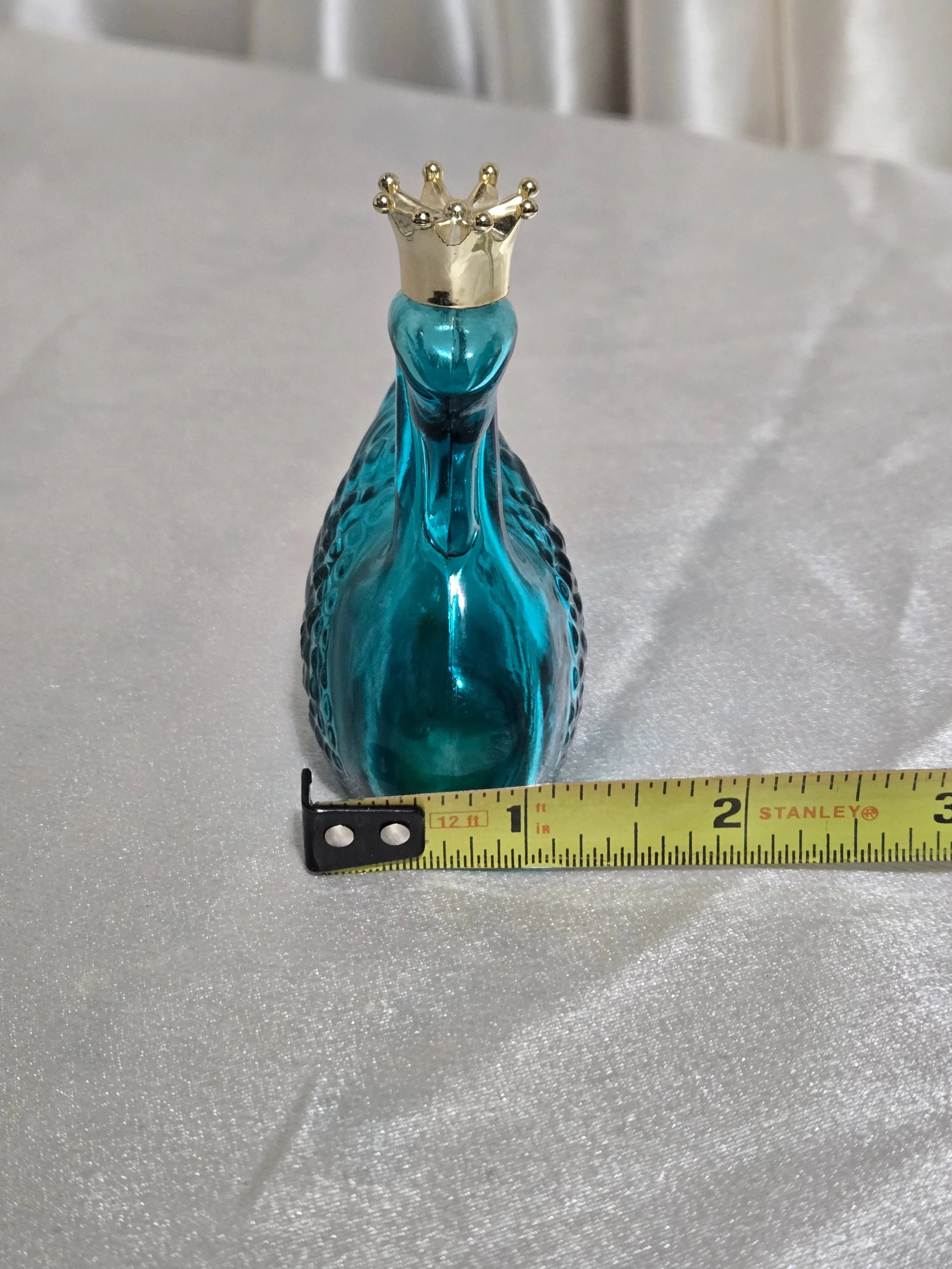 Vintage Avon swan perfume bottle in teal glass displayed with measuring tape for scale.