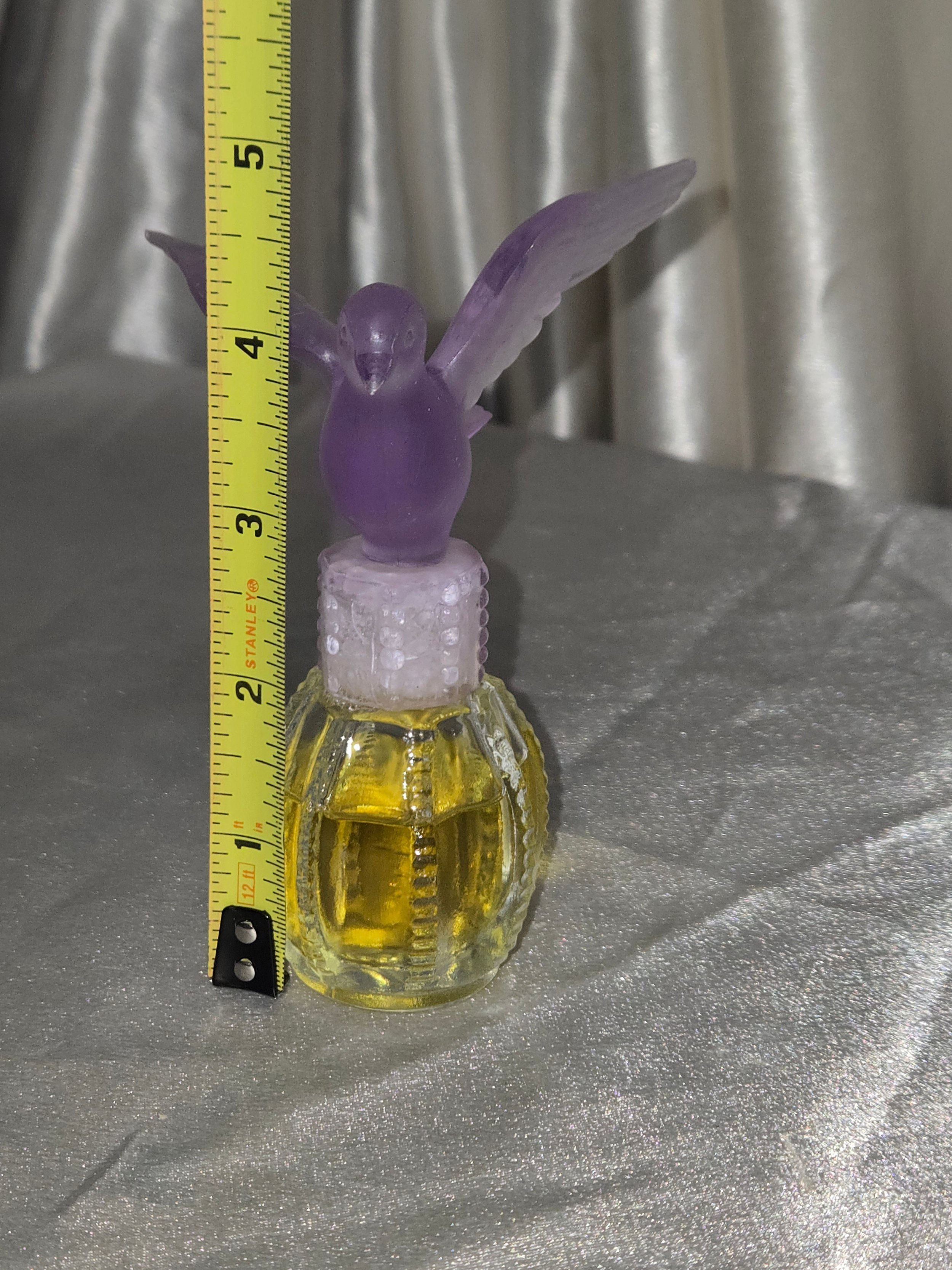 Vintage Avon purple dove perfume bottle displayed on satin backdrop with measuring tape for scale.