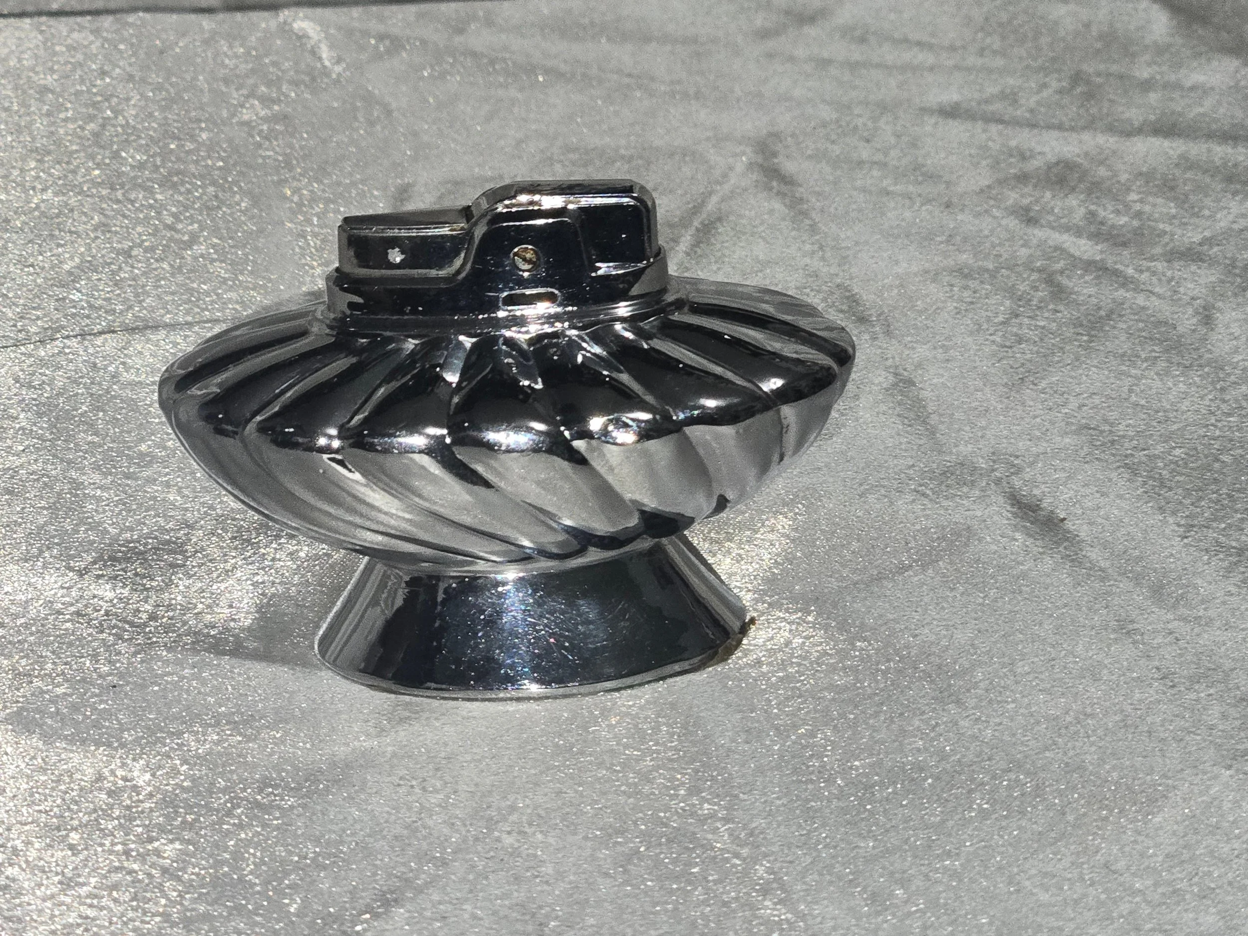 Vintage Ronson Regal chrome table lighter with swirl design, reflective silver finish, shown on silver backdrop.