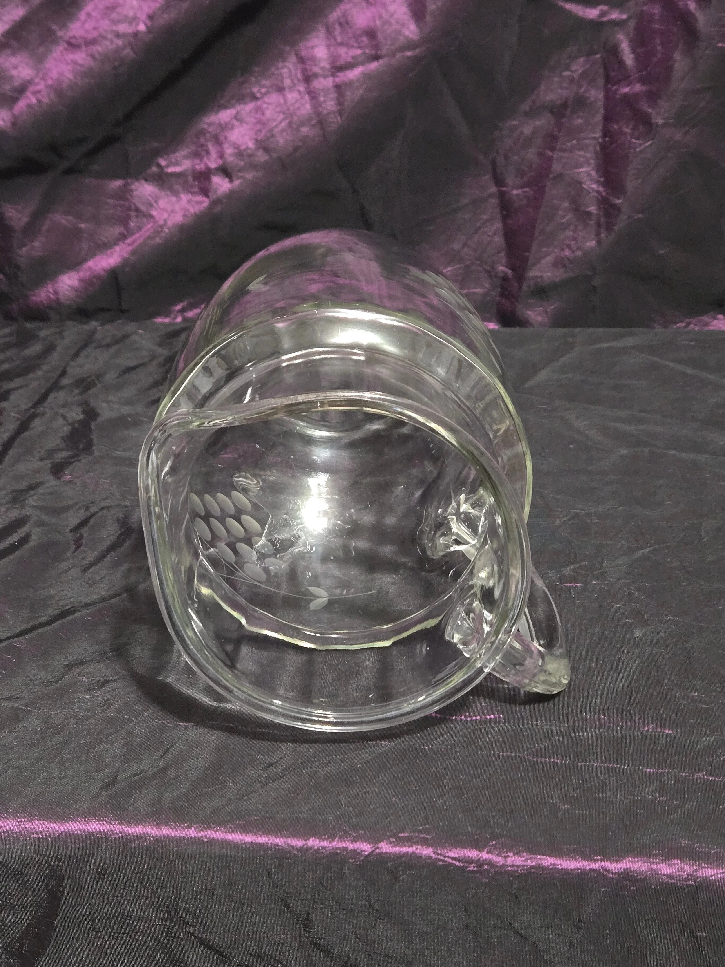 Clear glass pitcher etched with grapevine and crown designs, vintage mid-century style with curved handle and flared spout.