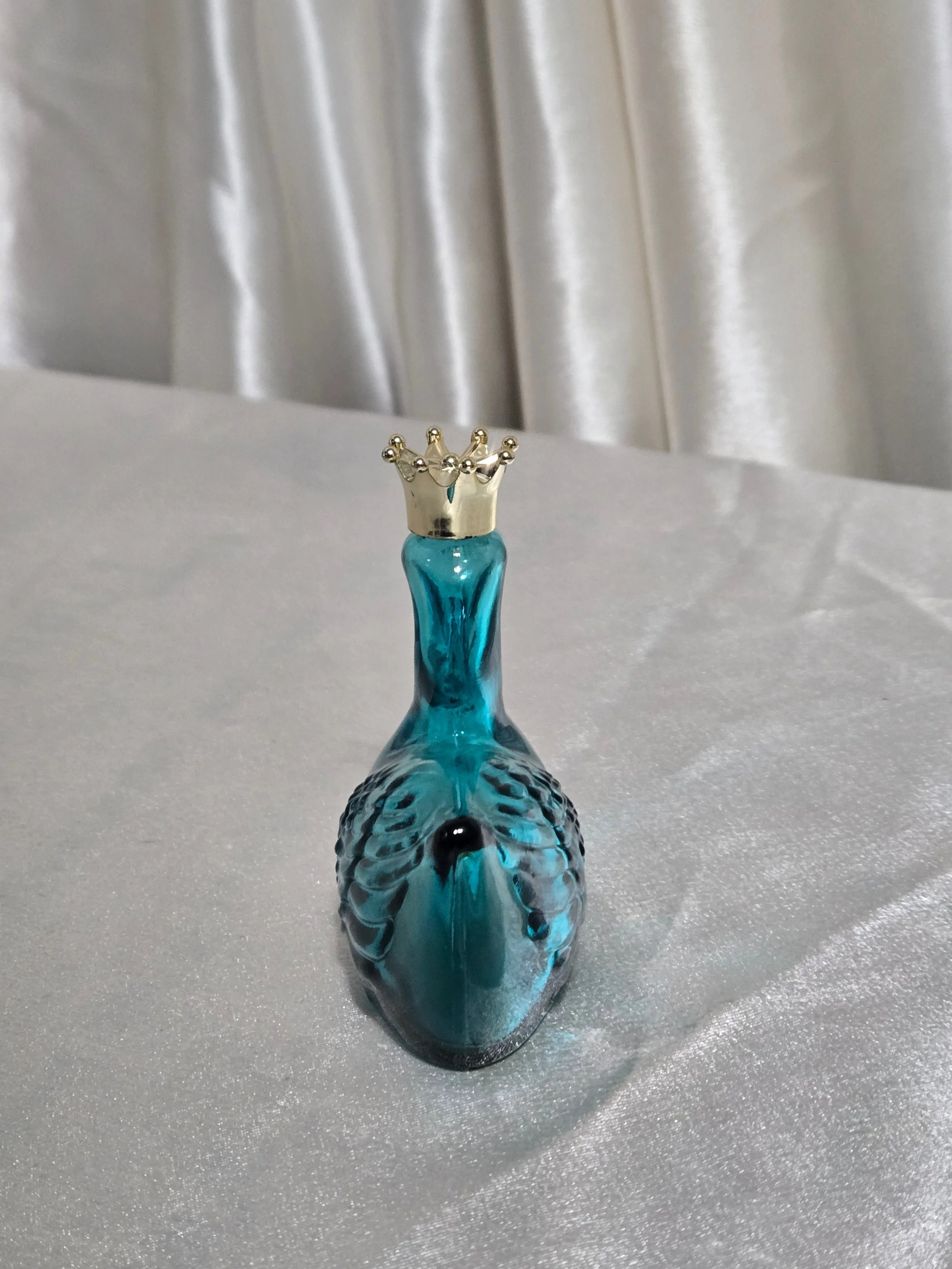 Close-up of gold crown stopper on vintage Avon teal swan glass perfume bottle.