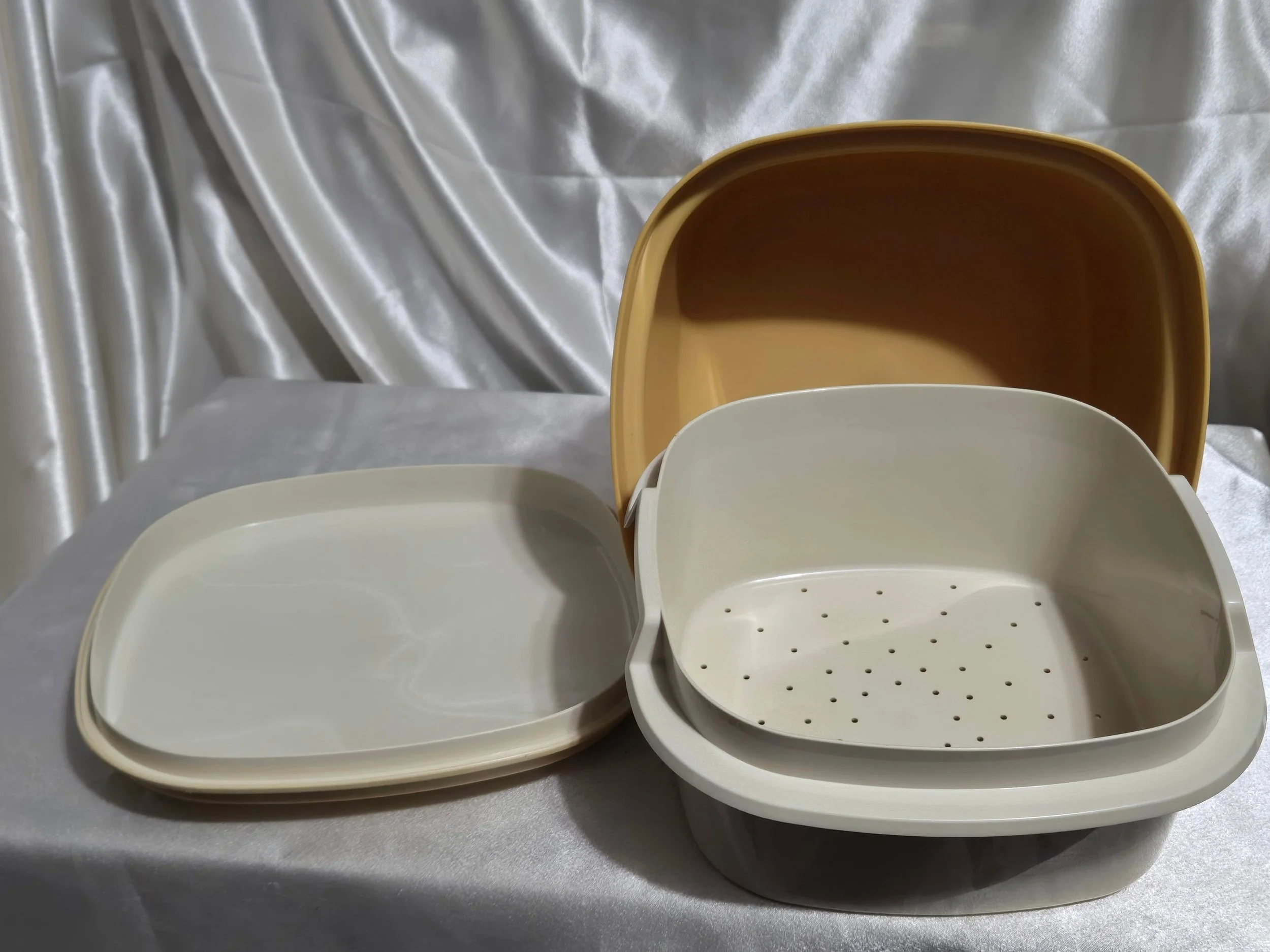 Vintage Tupperware microwave steamer in mustard yellow and ivory with lid removed and upside down, vented insert, and base on its side showing the inside.