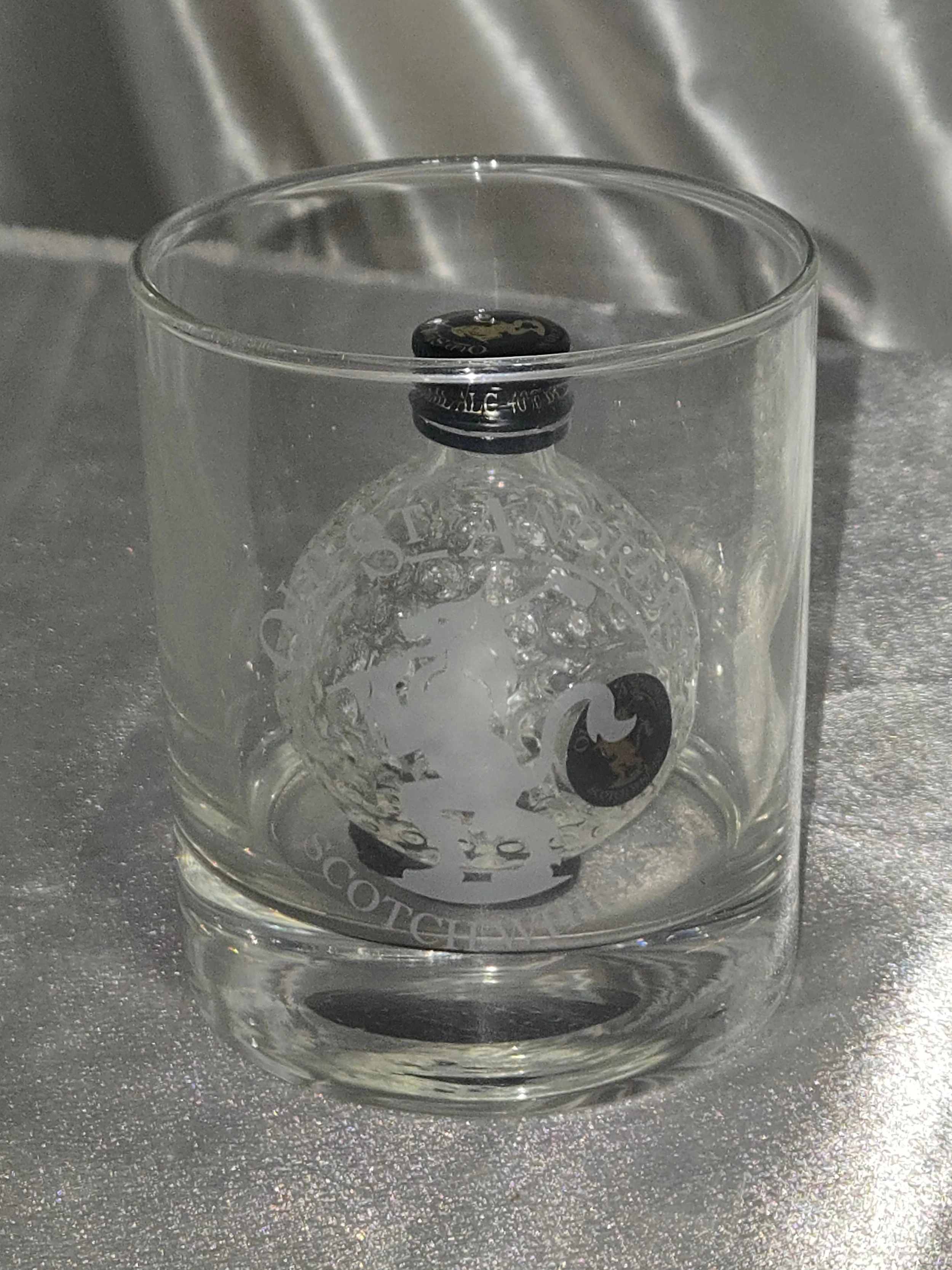 Side angle showing embossed golf ball texture of bottle inside rocks glass out of packaging