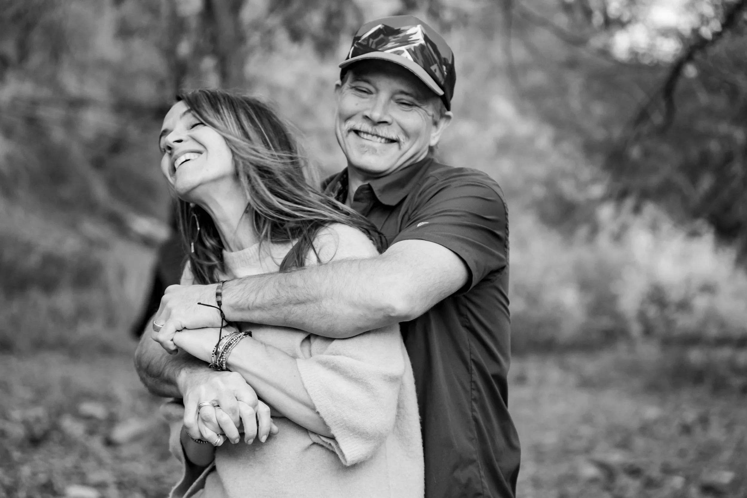 A man and woman laughing and embracing outdoors in black and white.
