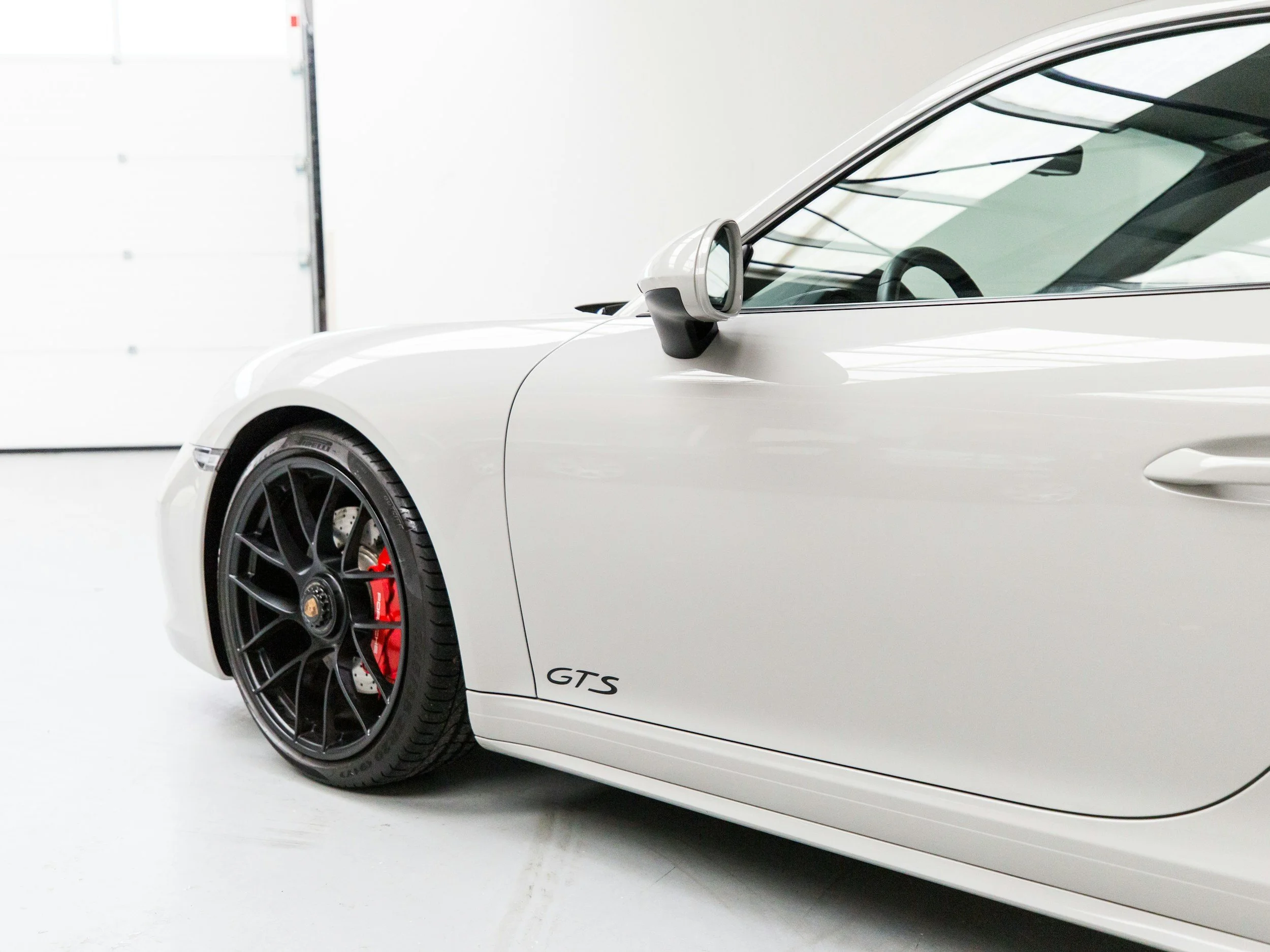 Witte Porsche GTS sportauto met zwarte velgen en rode remmen, binnen in een garage