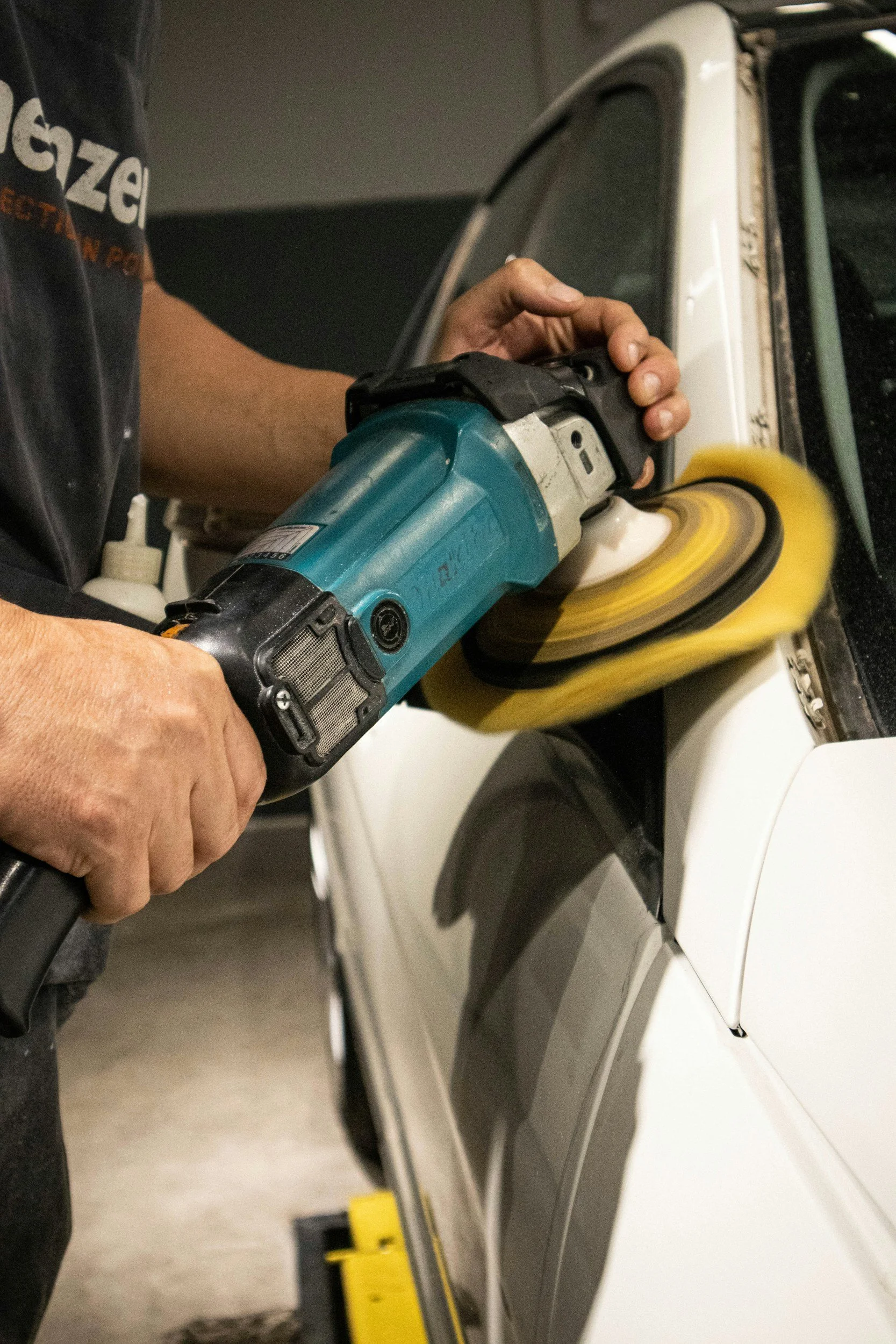 Persoon die een witte auto polijst met een elektrische polijstmachine met gele vacht.
