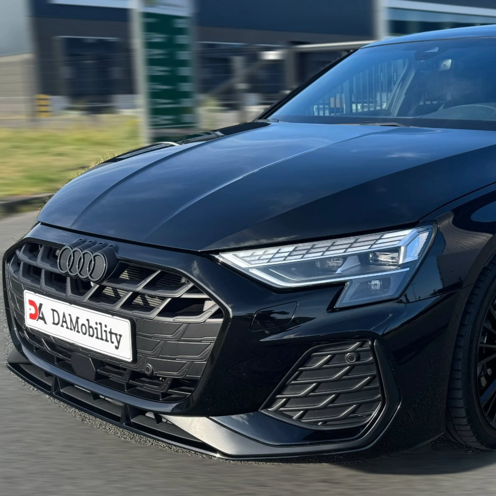 Zwarte Audi auto met DAmobility kentekenplaat, rijdend op de weg.