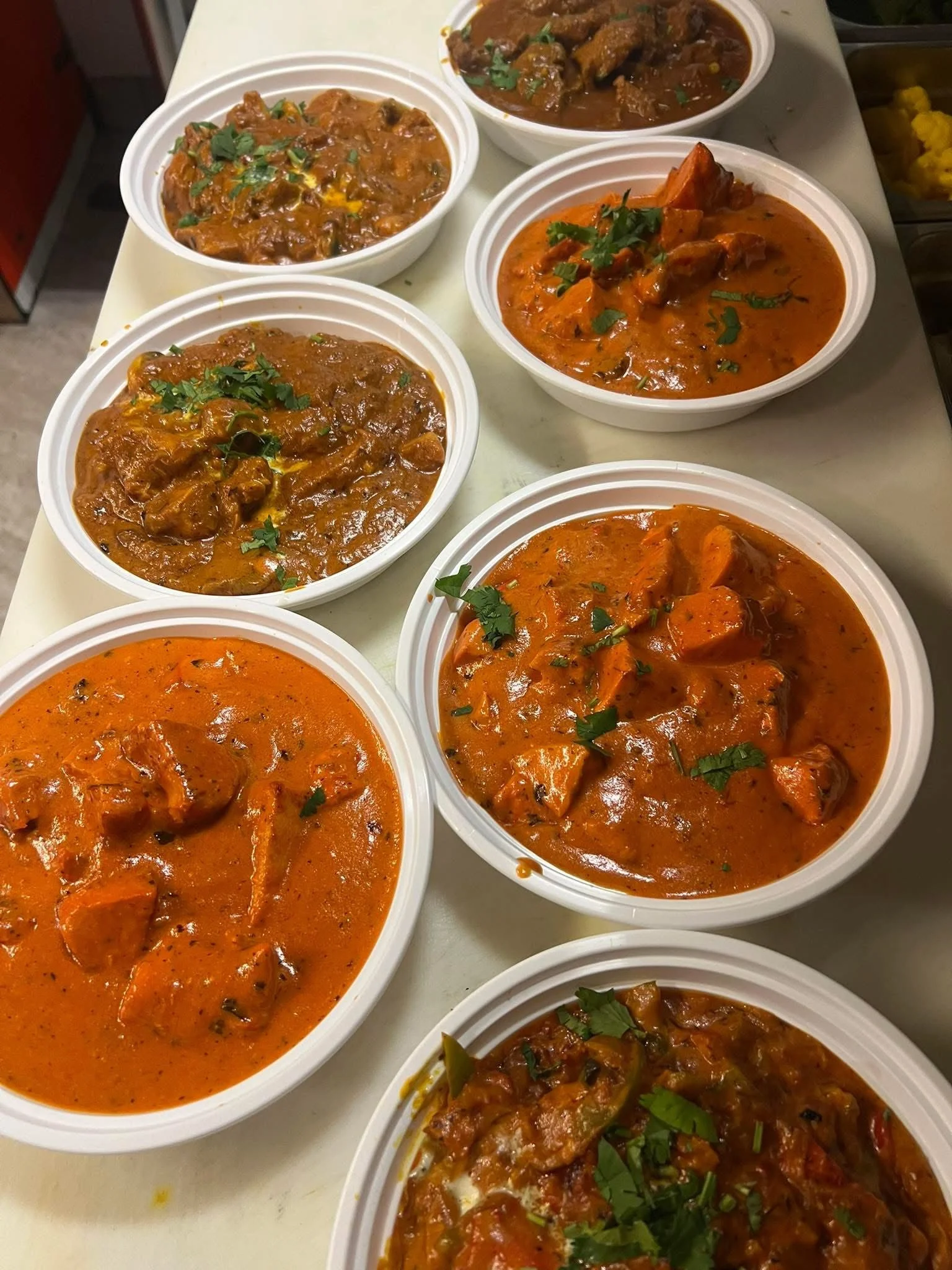 Several bowls of Indian curries with various meats and vegetables, garnished with cilantro, on a white tray.