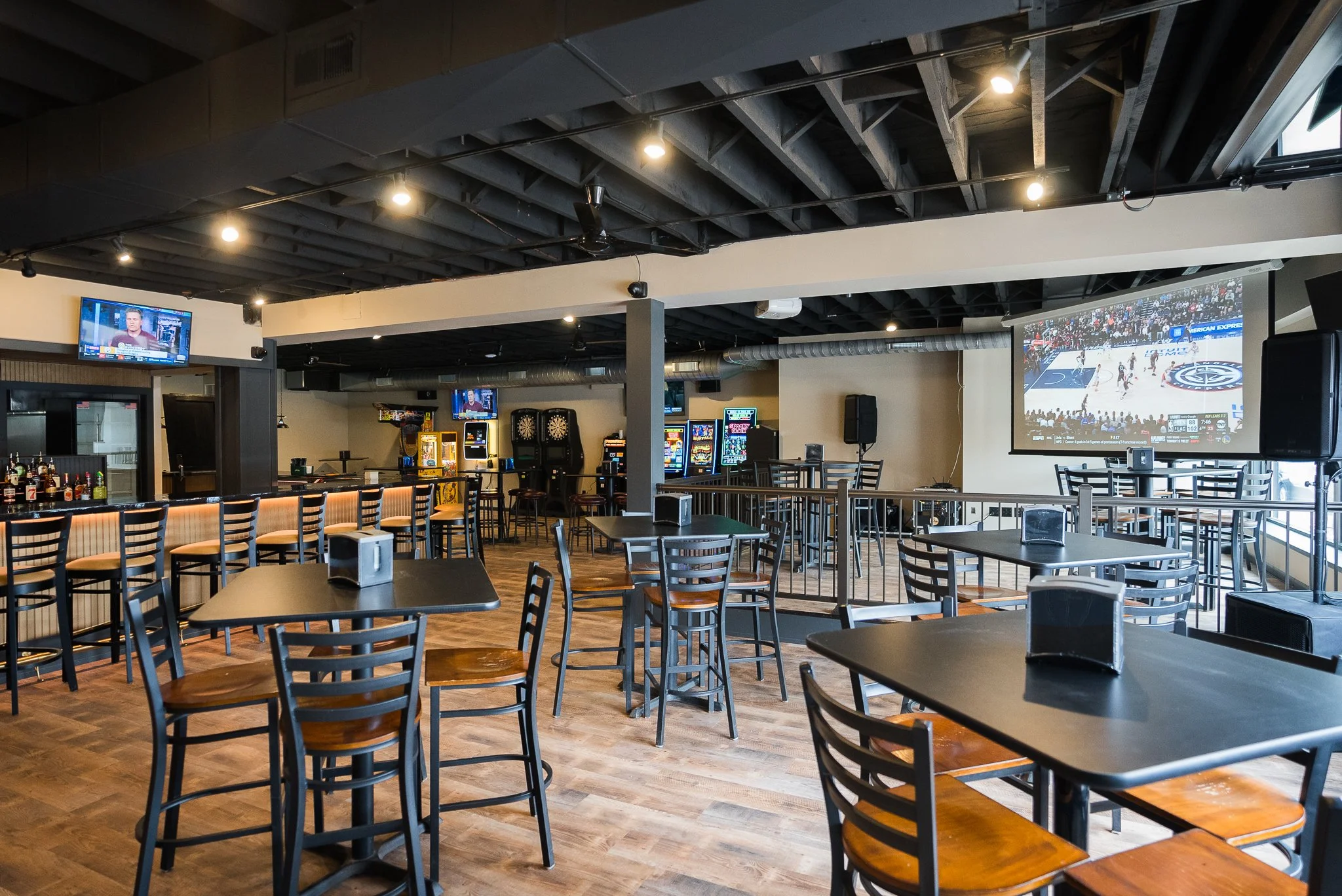 Interior of a sports bar with multiple tables and chairs, panasonic screens showing sports, and virtual golf game machines in the background. - The Rookery, La Crosse