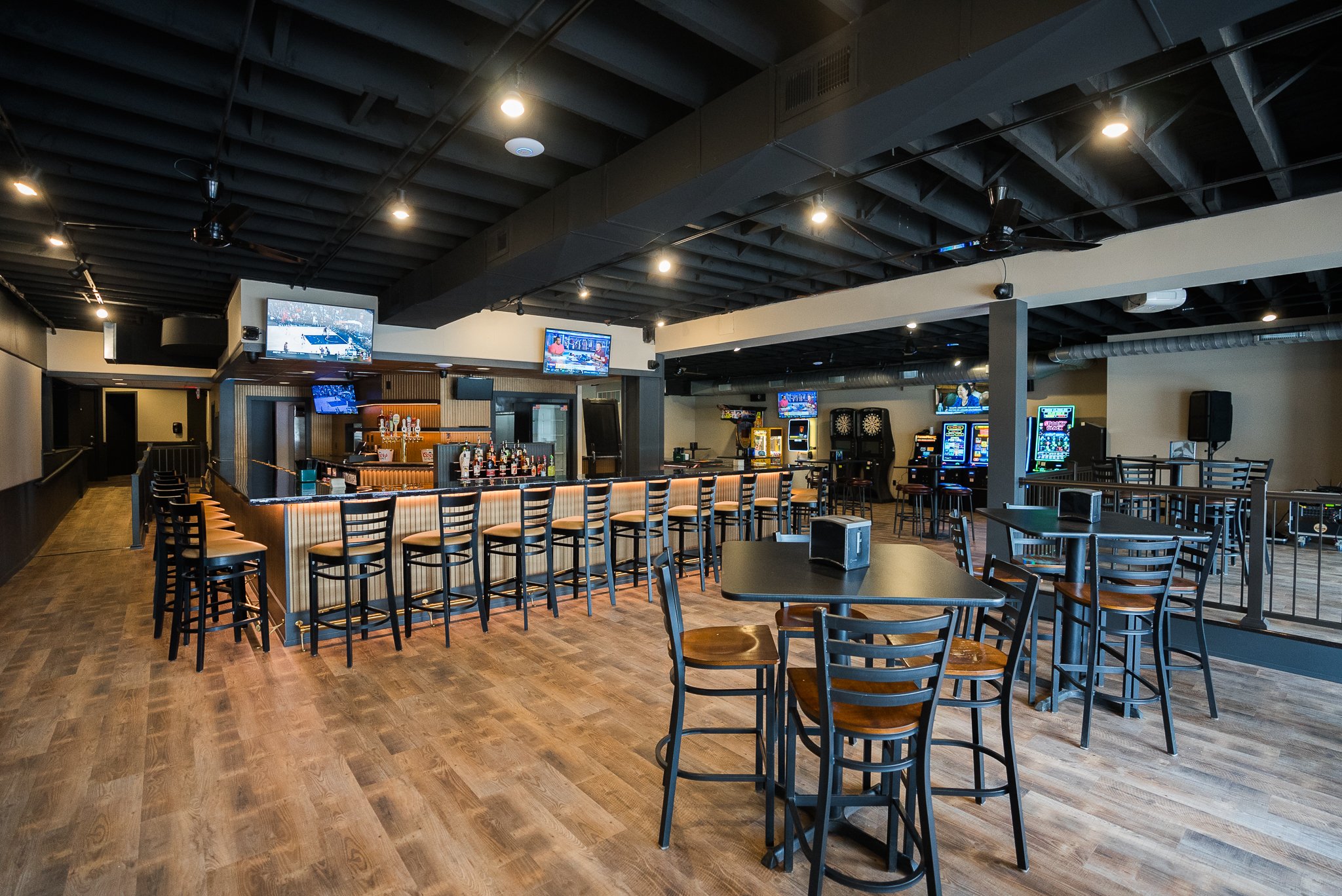 Empty bar and gaming area with tables, chairs, and multiple electronic gaming machines in a modern lounge.