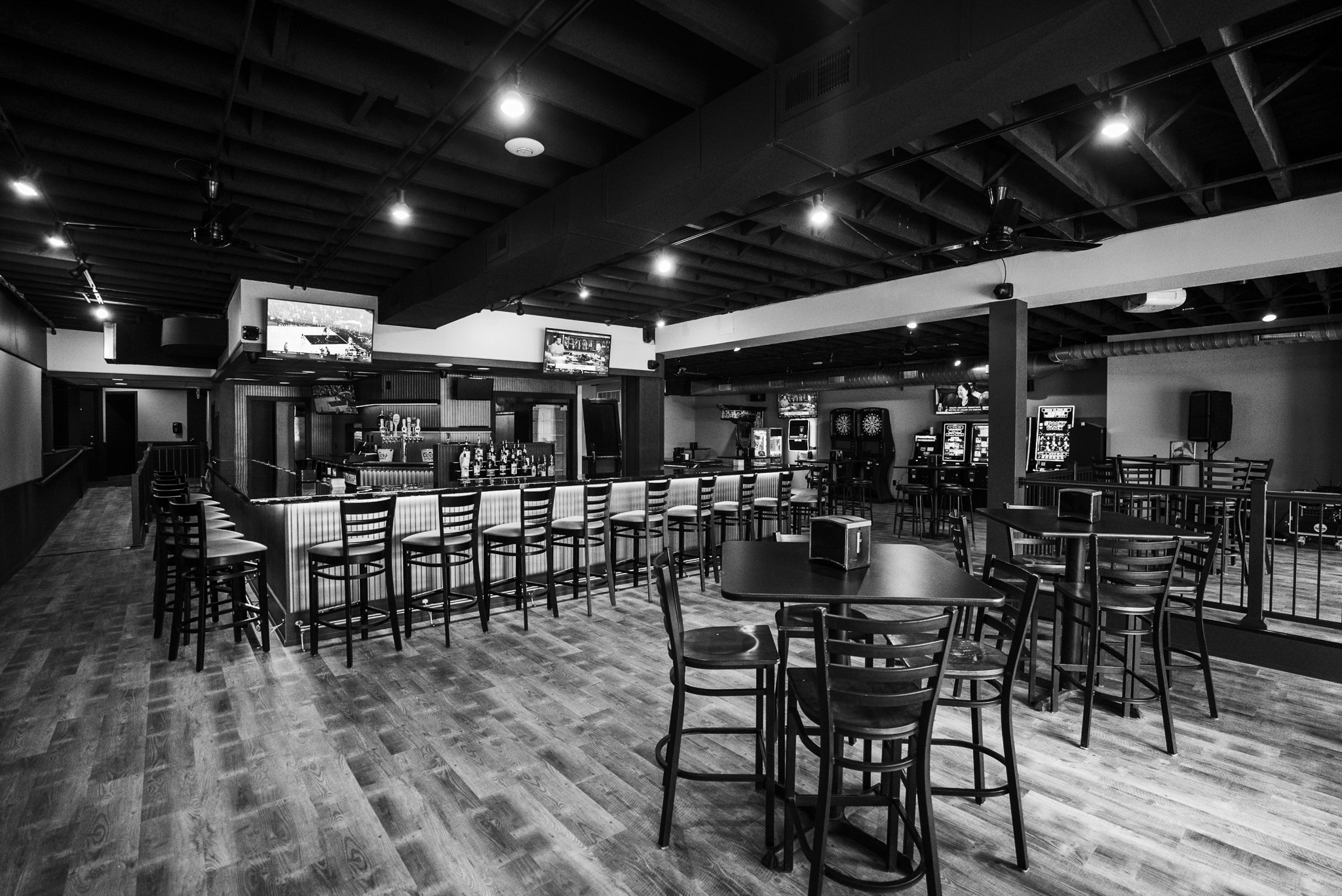 Empty bar and game area with arcade machines and dartboards in a black and white lounge - The Rookery