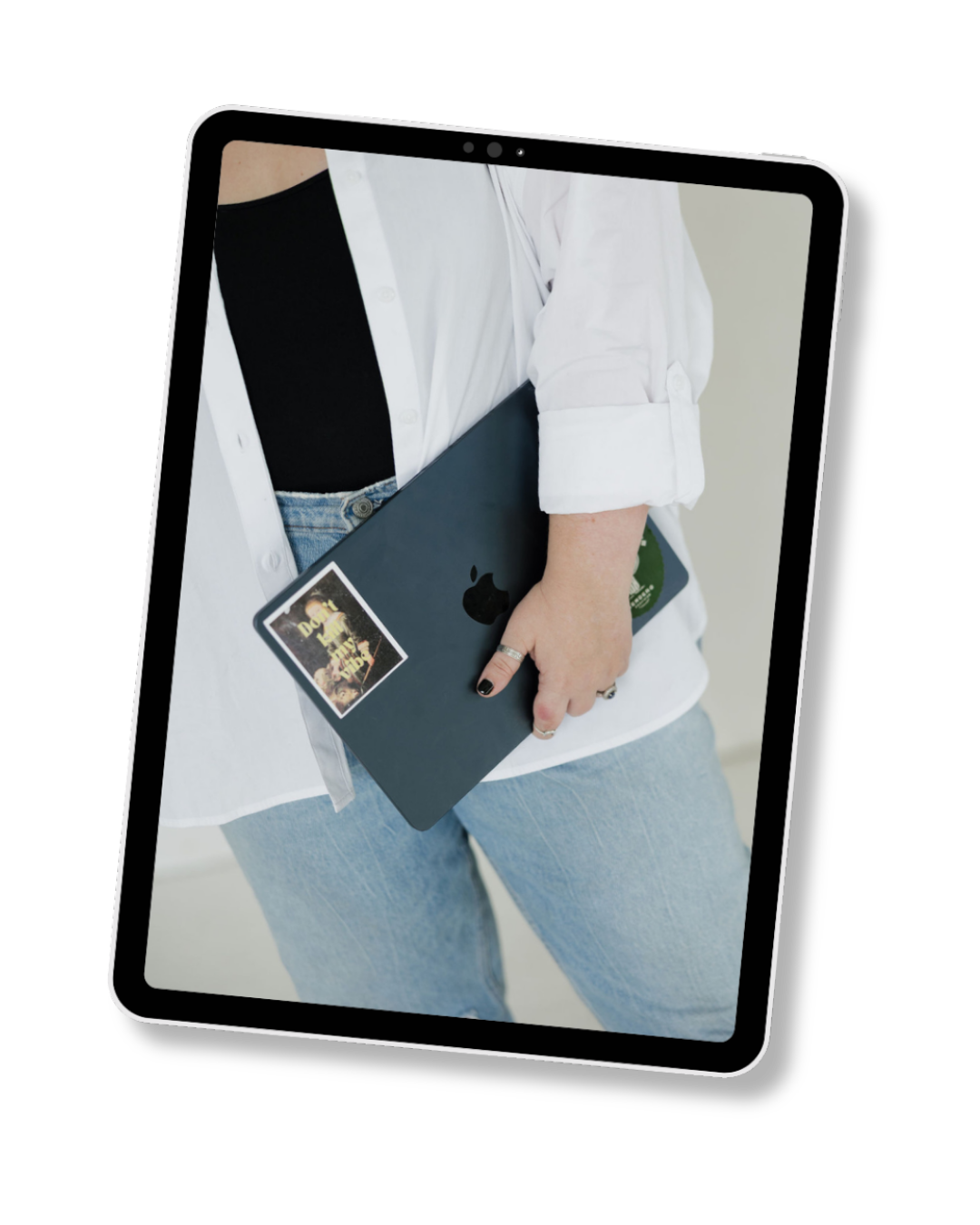 Woman holding laptop. White button-up shirt, black shirt, blue jeans, and black nail polish with rings.