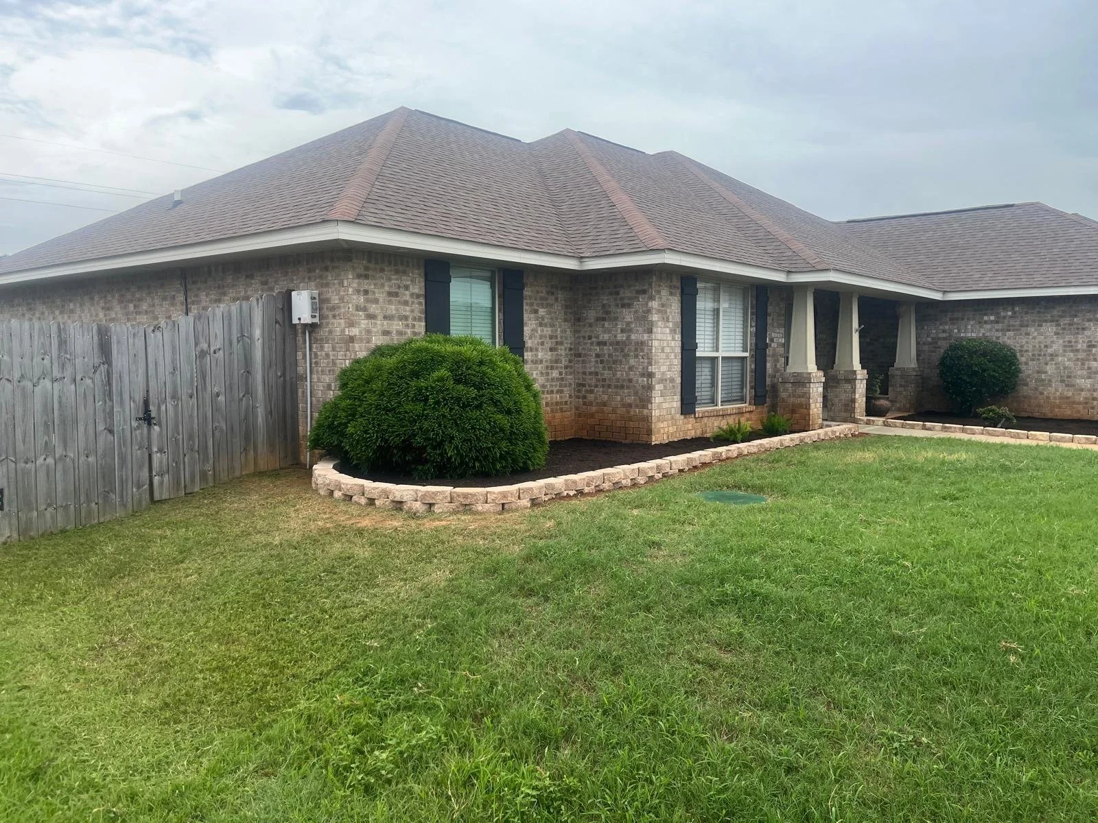 A brick house with a gabled roof, bay window, and porch, surrounded by a well-maintained lawn and landscaped bushes.