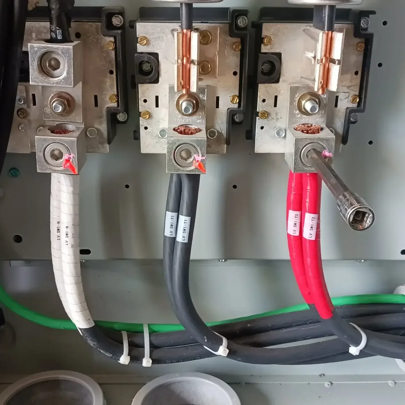 Electrical wiring and connections inside an electrical panel, including cables with white, black, and red insulation connected to metal contact points.