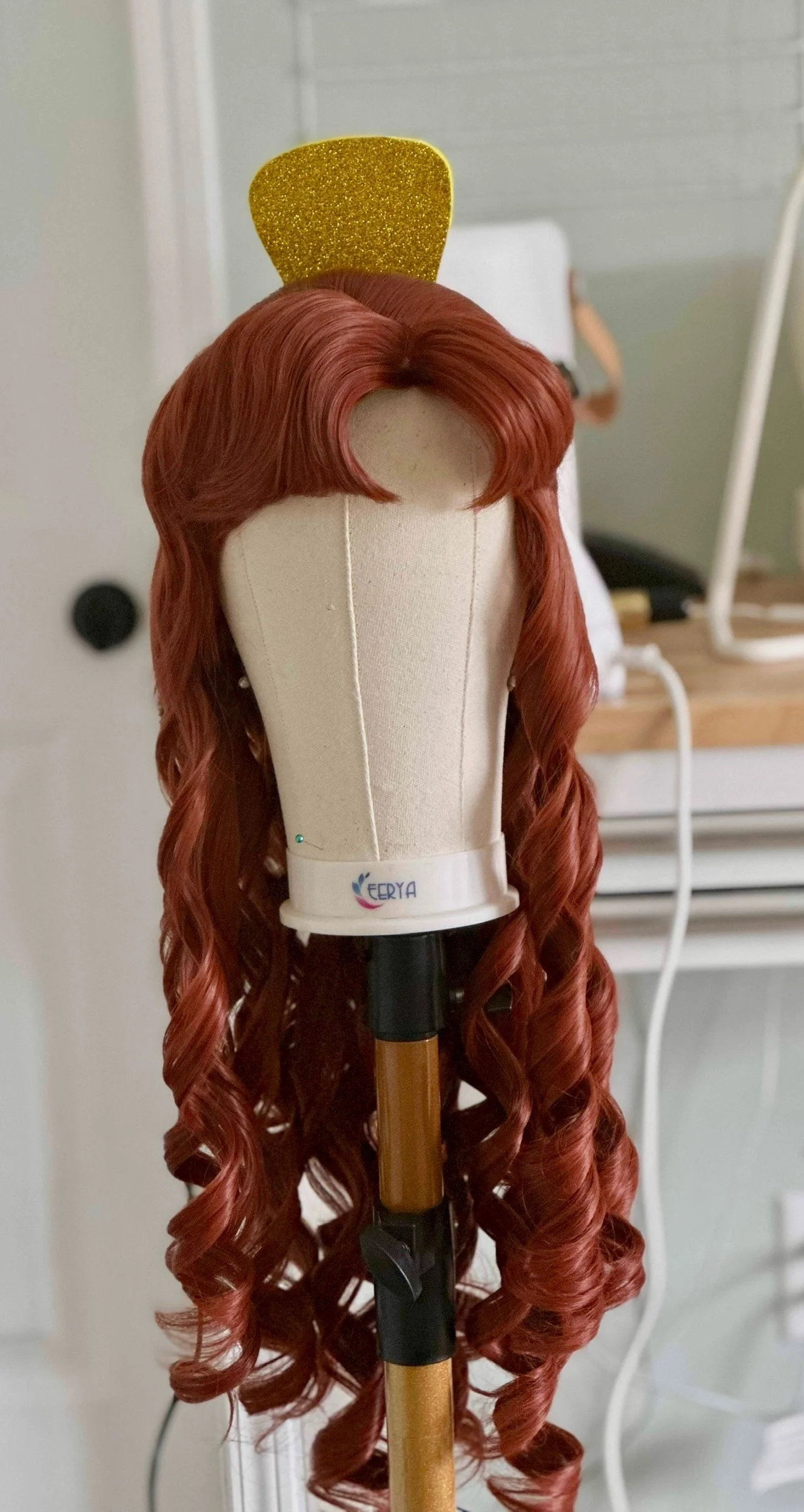 A mannequin head with long, curly, red hair and a yellow glitter headband.