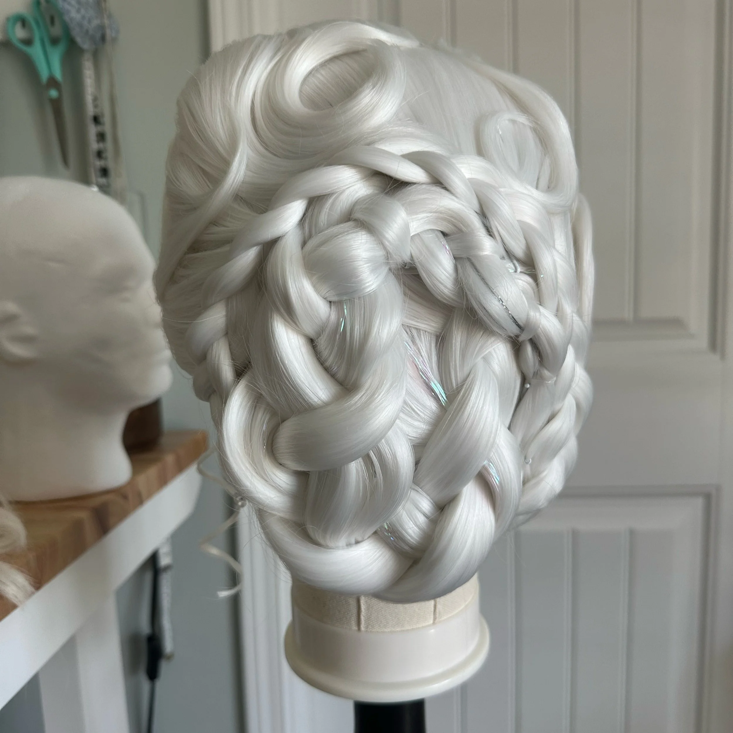 A wig with long, platinum blonde hair styled in intricate, thick braids wrapped around each other, displayed on a mannequin head.