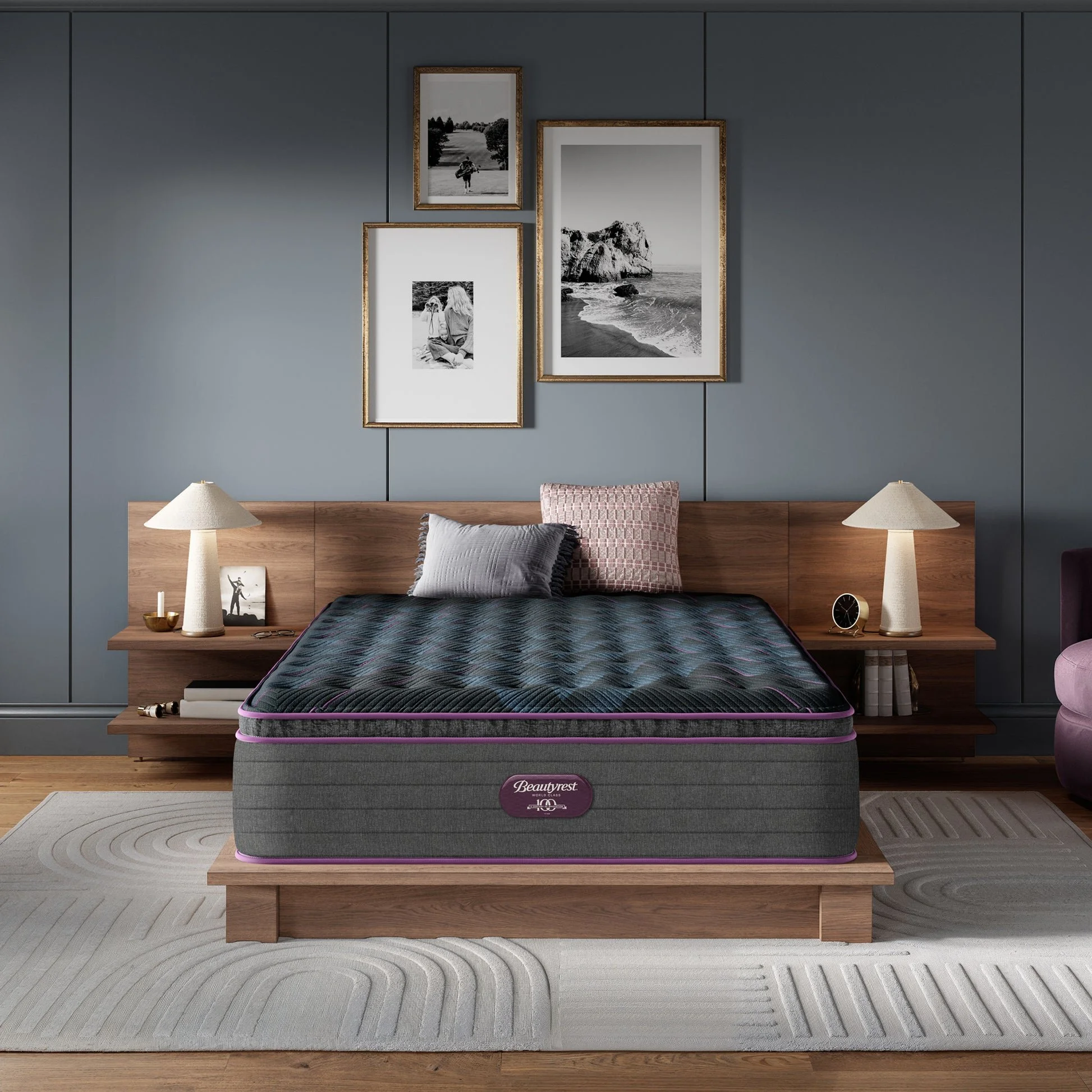 A bedroom with a wooden bed frame and mattress, two side tables with matching lamps, and framed black and white photographs on a blue wall.