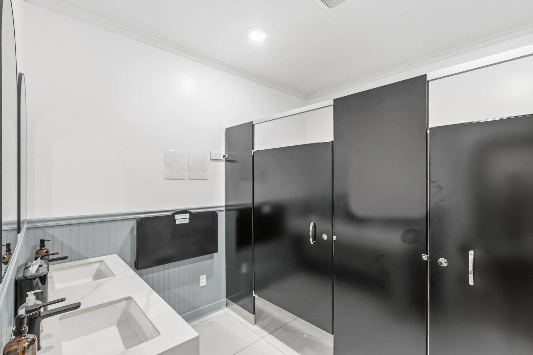 Public restroom with double sinks, black and white color scheme, and black stall doors.