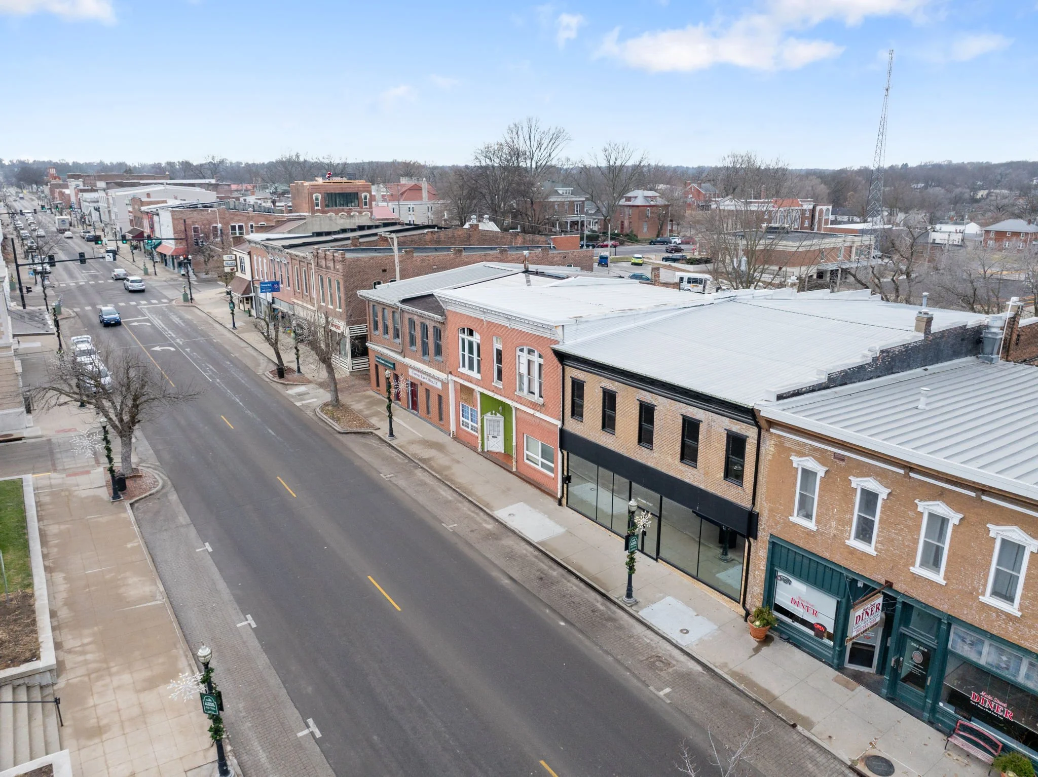 Empty downtown street with shops and restaurants, leafless trees, cloudy sky, and distant hills.
