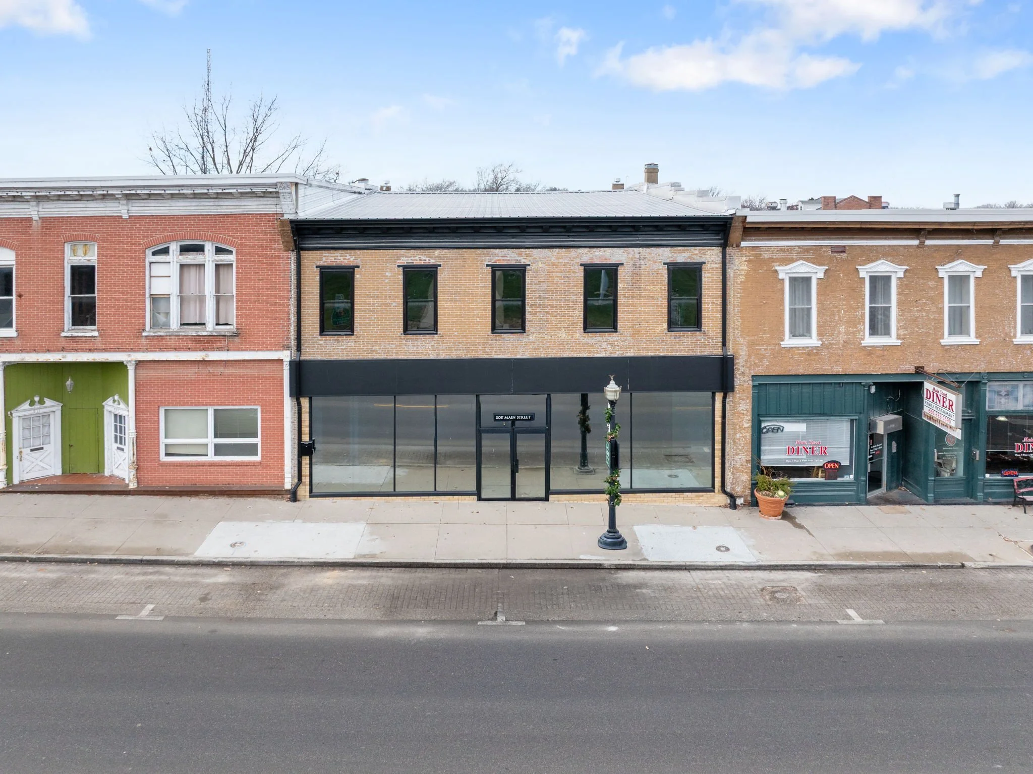 Empty storefront on Main Street with a black facade, large glass windows, and a glass door. A streetlamp decorated with greenery is in front of the store.