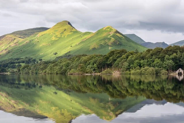 Green mountains reflecting in a calm lake with a cloudy sky overhead.