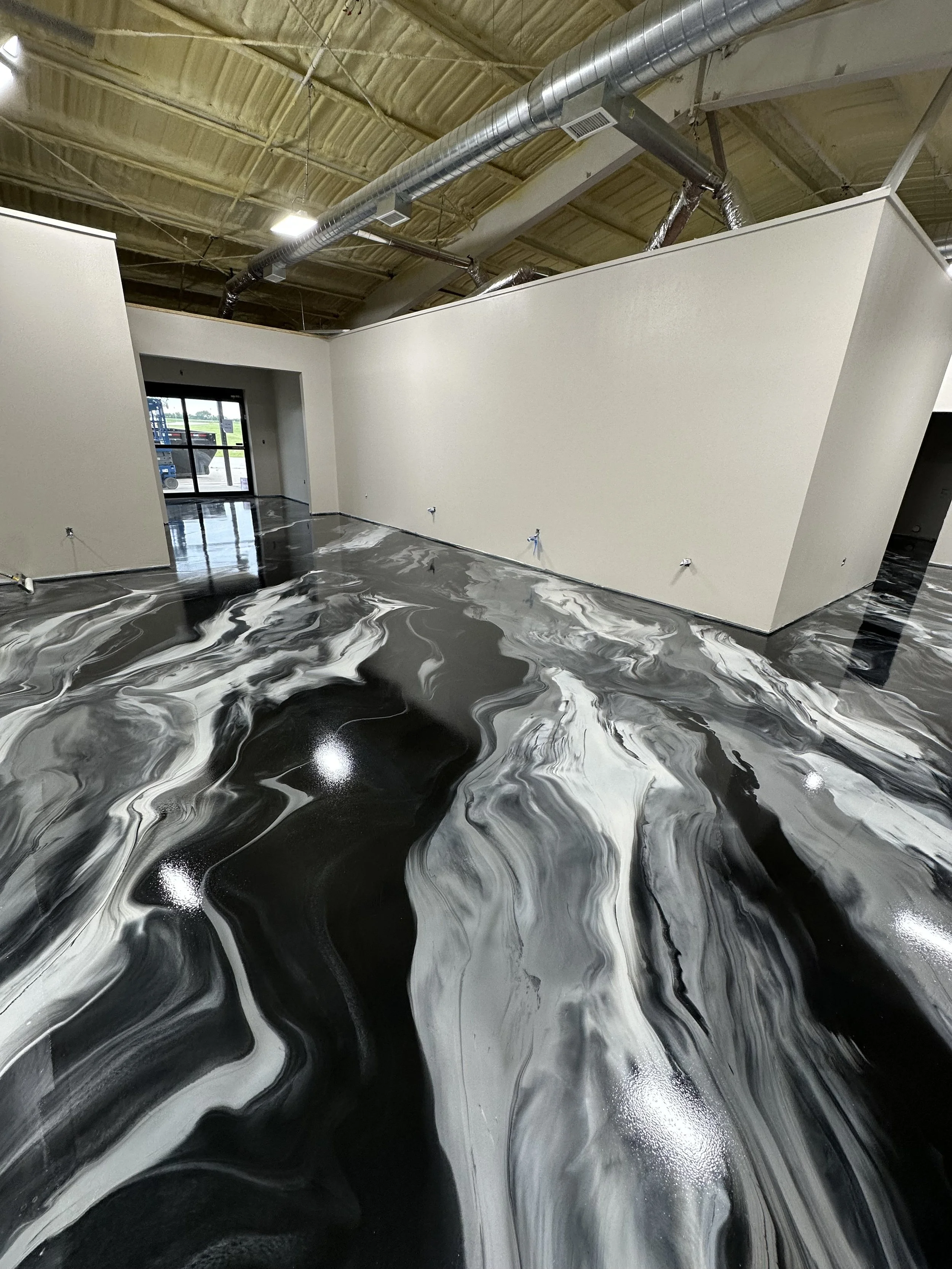 Interior of a commercial building with a polished black and white marbled floor, plain white walls, exposed ductwork, and unfinished ceiling.