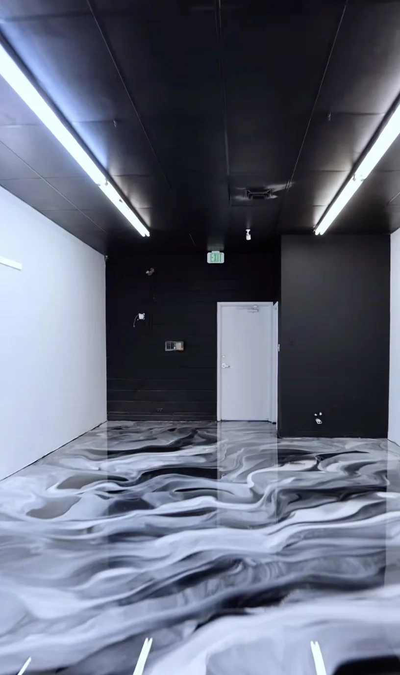 Empty room with black ceiling, white walls, black wall with a door, and a floor with black, white, and gray swirling marble pattern.