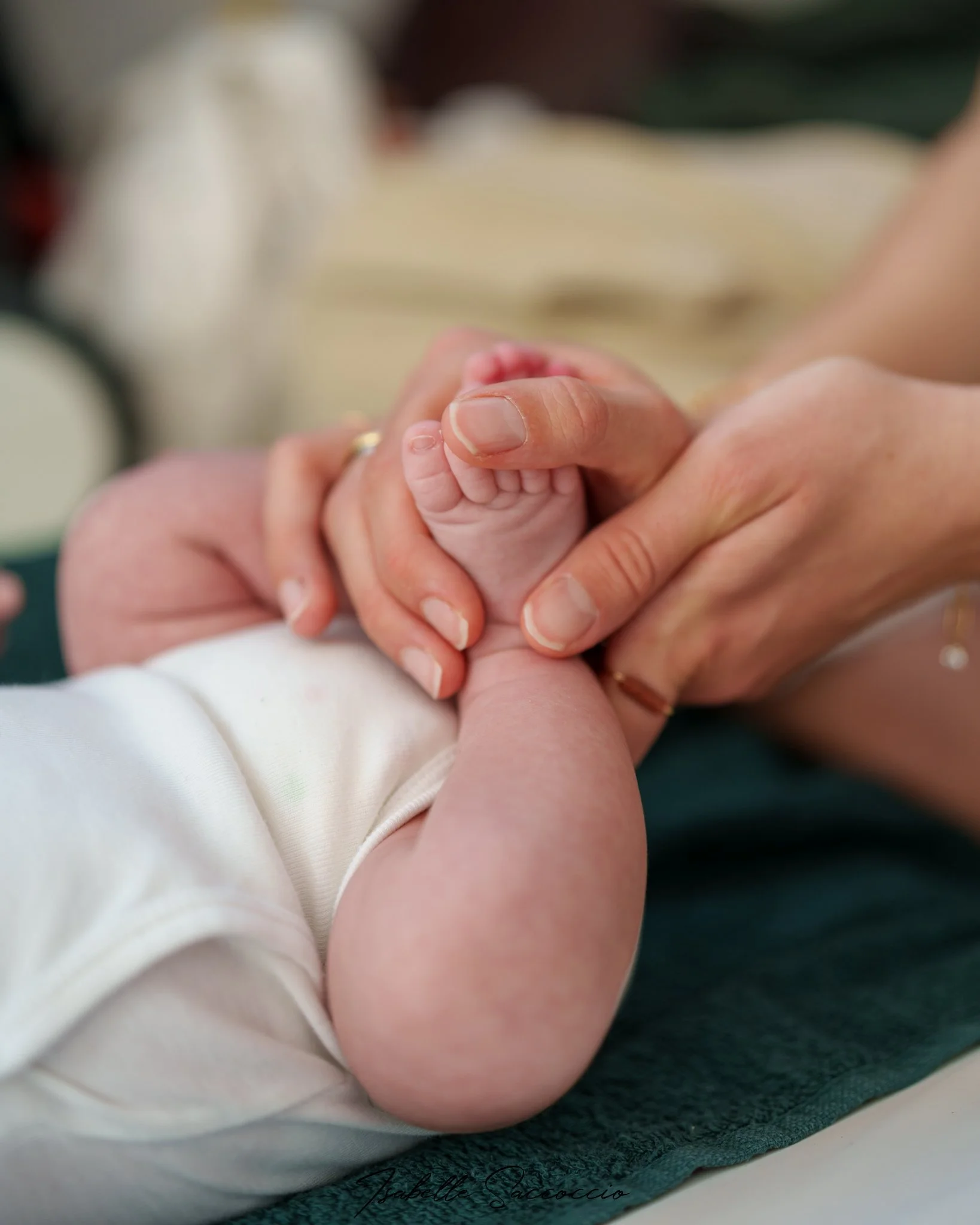 Un parent qui masse le pied de son bébé,  gros plan sur la main du bébé et la main du parent, fond flou.