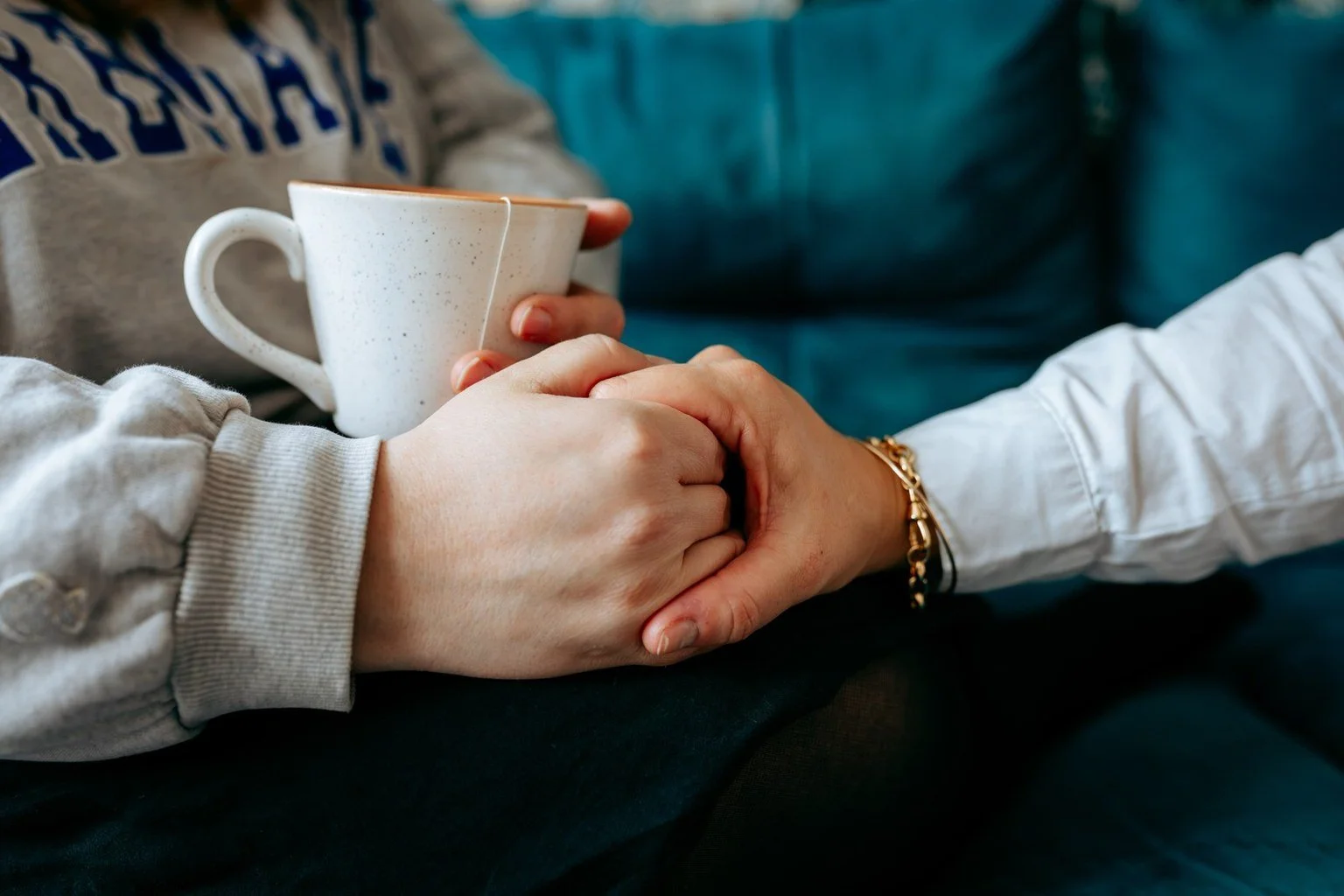 Deux personnes tiennent la main l'une de l'autre, avec une tasse de café ou de thé en arrière-plan.