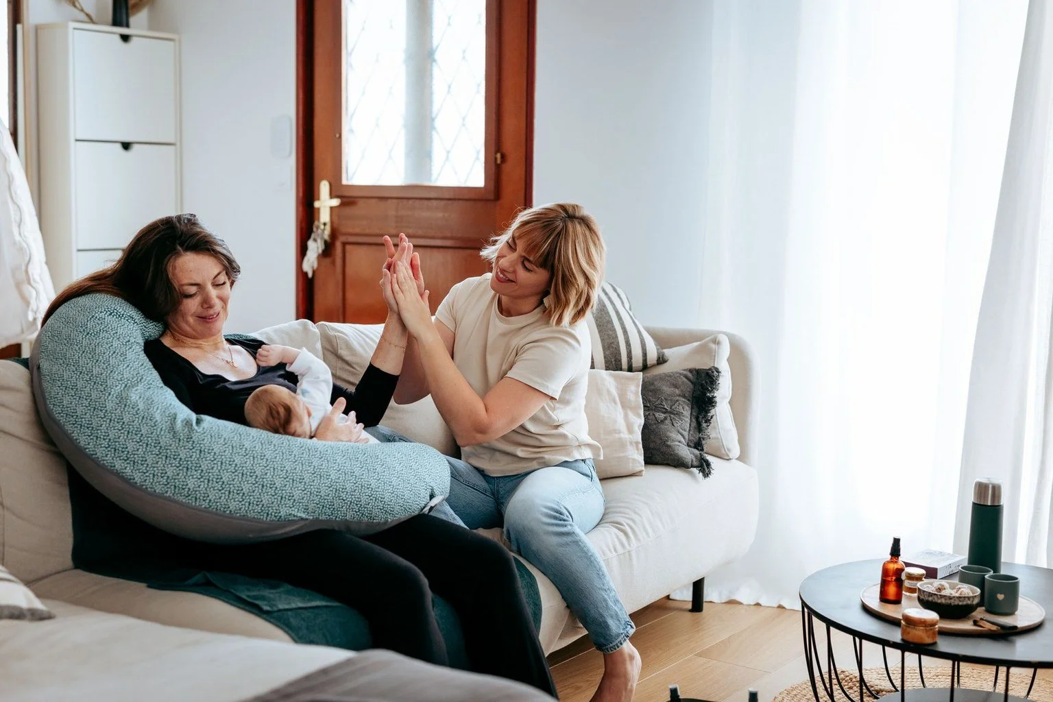 Deux femmes et un bébé dans un salon, elles se donnent un high-five, ambiance chaleureuse et conviviale.