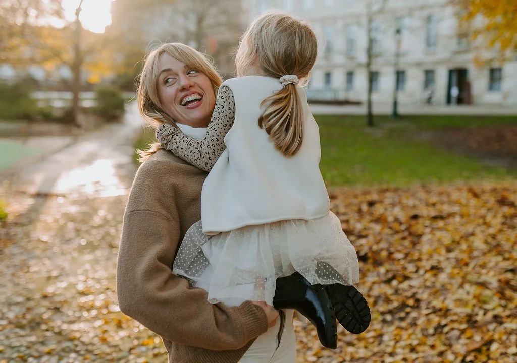 Une femme souriante tient une jeune fille dans ses bras dans un parc en automne.