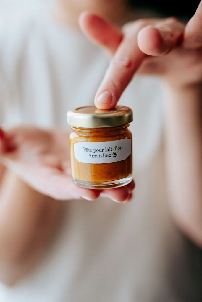 Une personne tient un petit pot en verre avec un étiquette portant la mention "Pâte pour lait d'or Amandine". Golden latte, la boisson régénérante et réconfortante.
