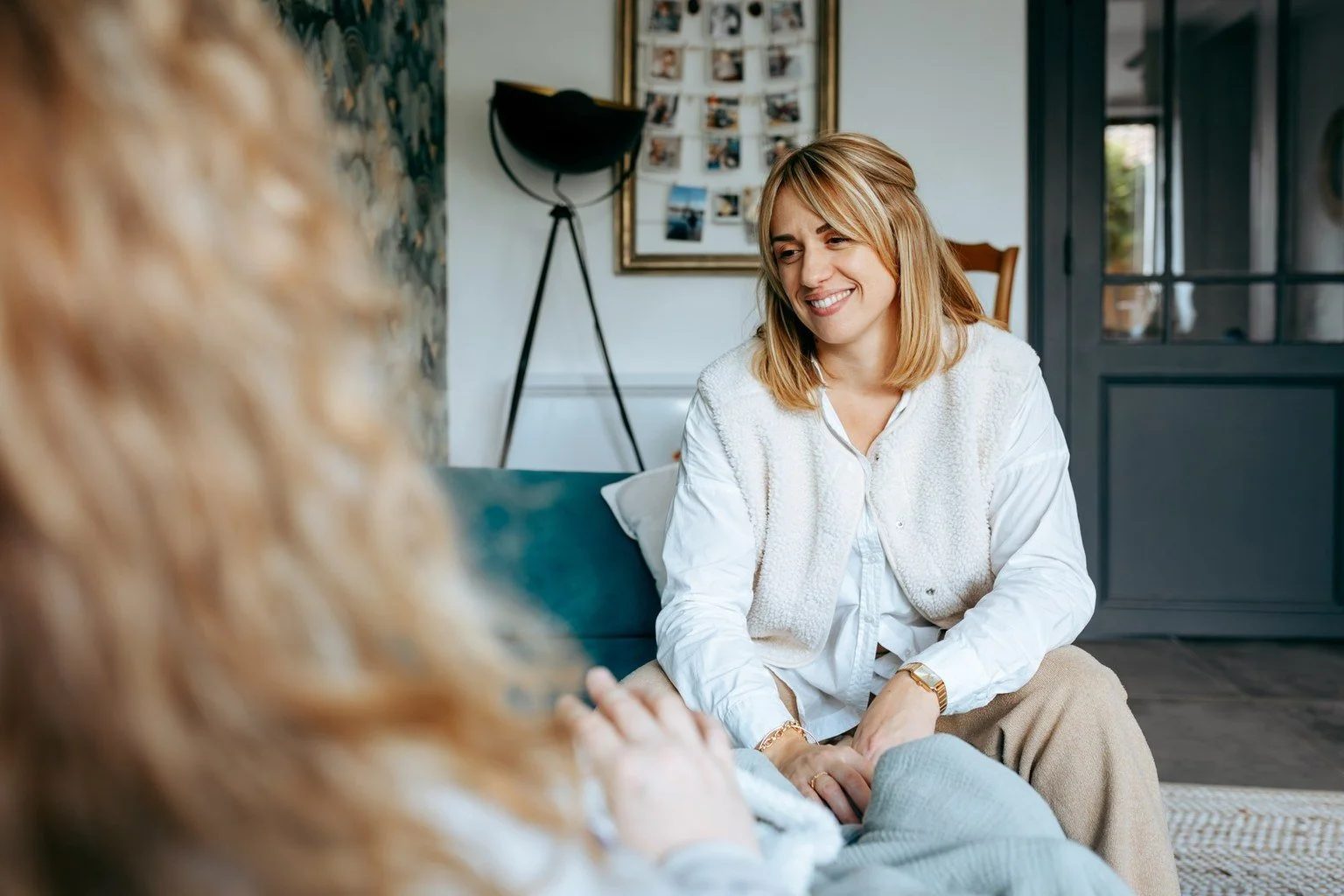 Deux femmes assises dans un salon, discutant et se souriant. L'une est une mère , l'autre , sa doula.