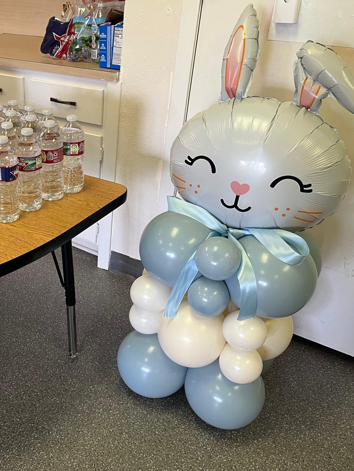 Foil balloon bunny rabbit with a blue, and cream balloon stack base, and a blue ribbon neck tie. 