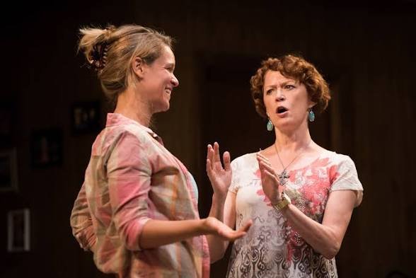 Two women having a conversation, one smiling and the other appearing surprised, indoors with a dark background. Byhalia, Mississippi CATF Actresses Jessica and Hollis playwight: Evan