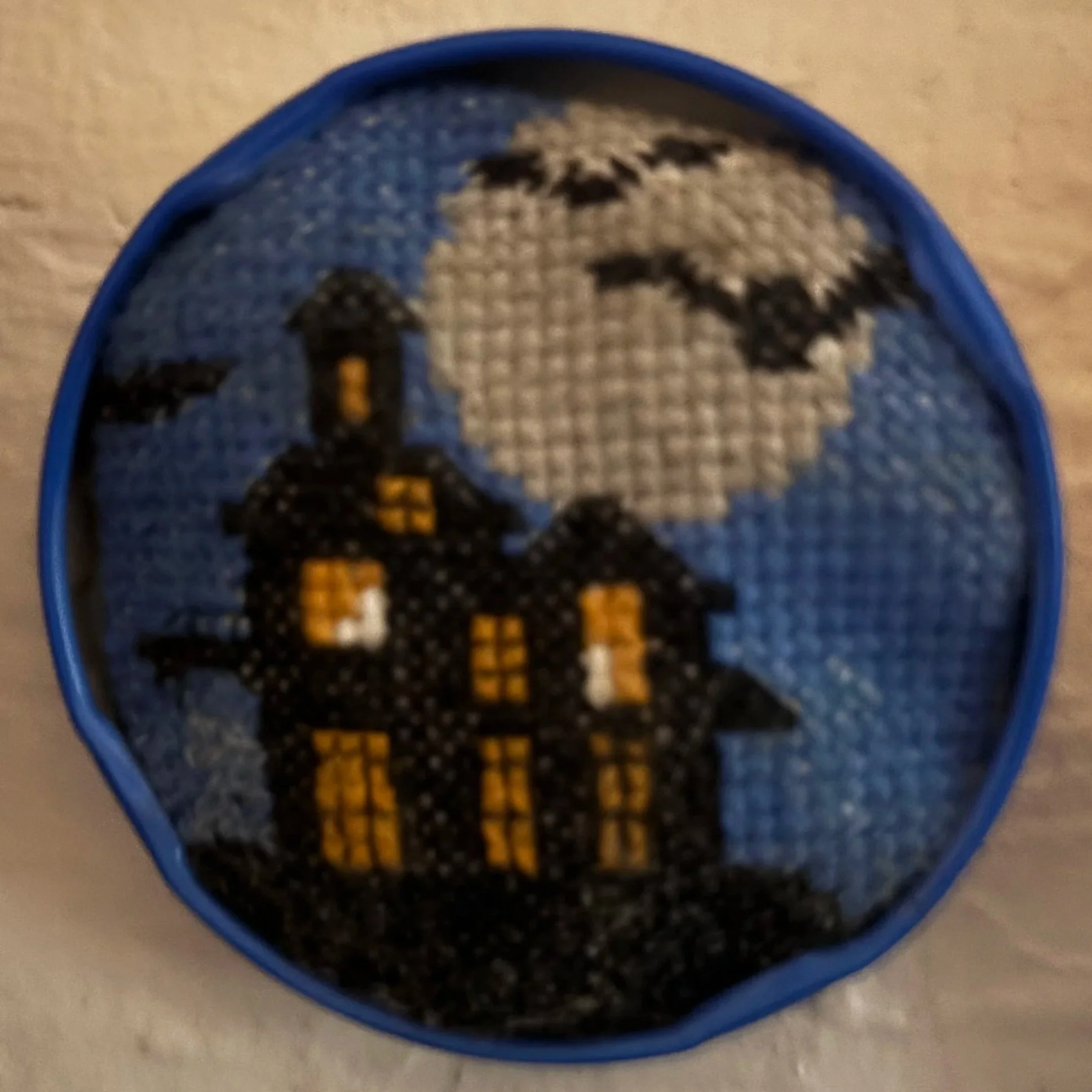 Cross-stitch pattern of a haunted house and moon with clouds, in a circular frame.
