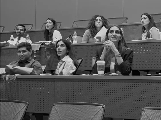 Group of diverse students sitting in a lecture hall with notebooks and water bottles, attentively listening.