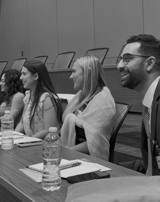 Group of diverse young adults sitting at a conference table, smiling and paying attention during a meeting in a modern conference room.