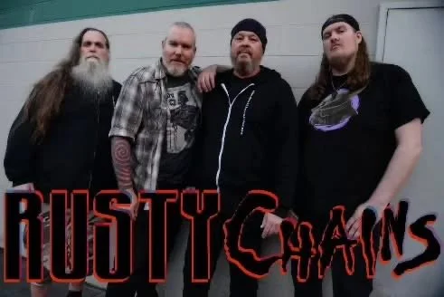 Four men standing together against a wall, with a logo that says 'Rusty Chains' in red and black at the bottom.