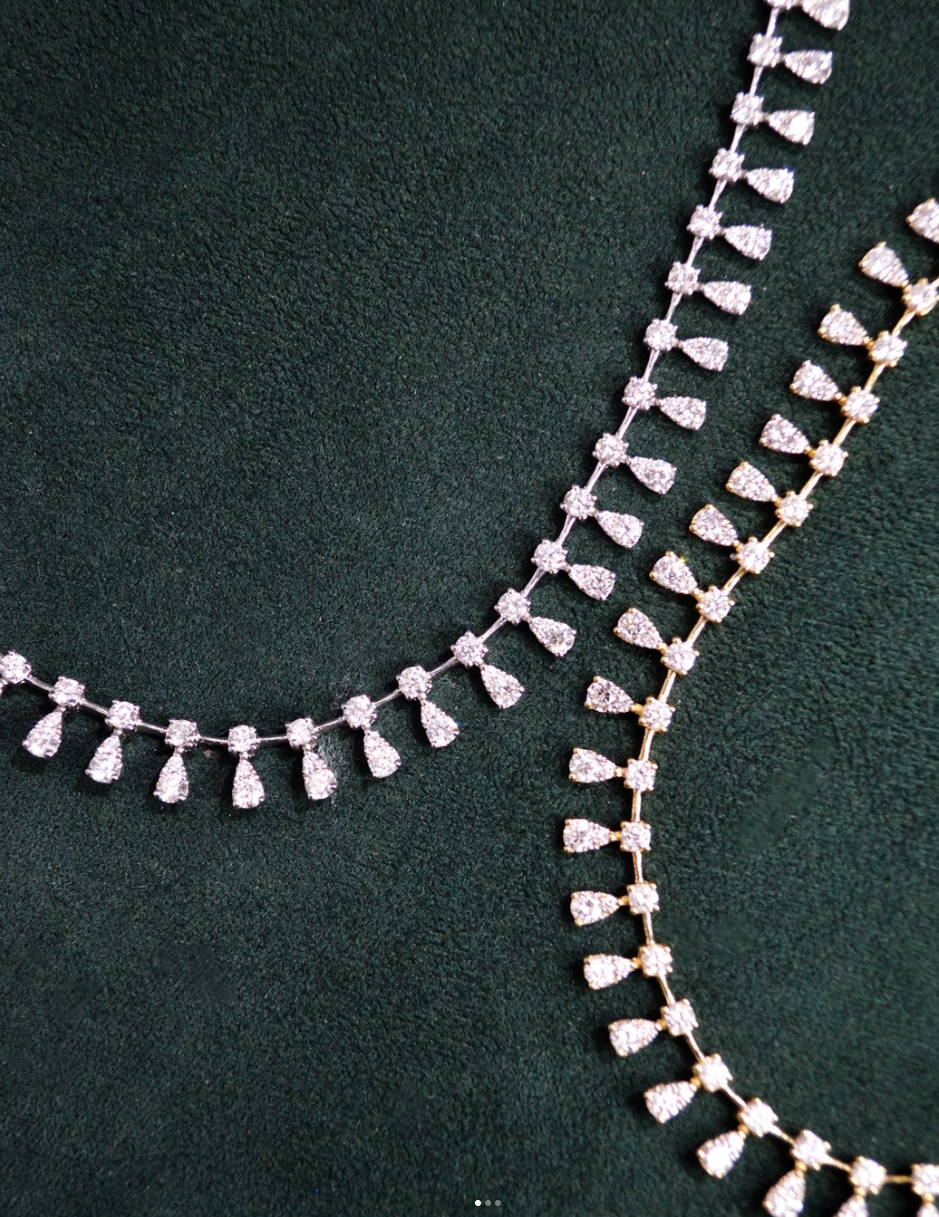Close-up of two diamond necklaces with matching diamond drop pendants, displayed on dark green fabric.