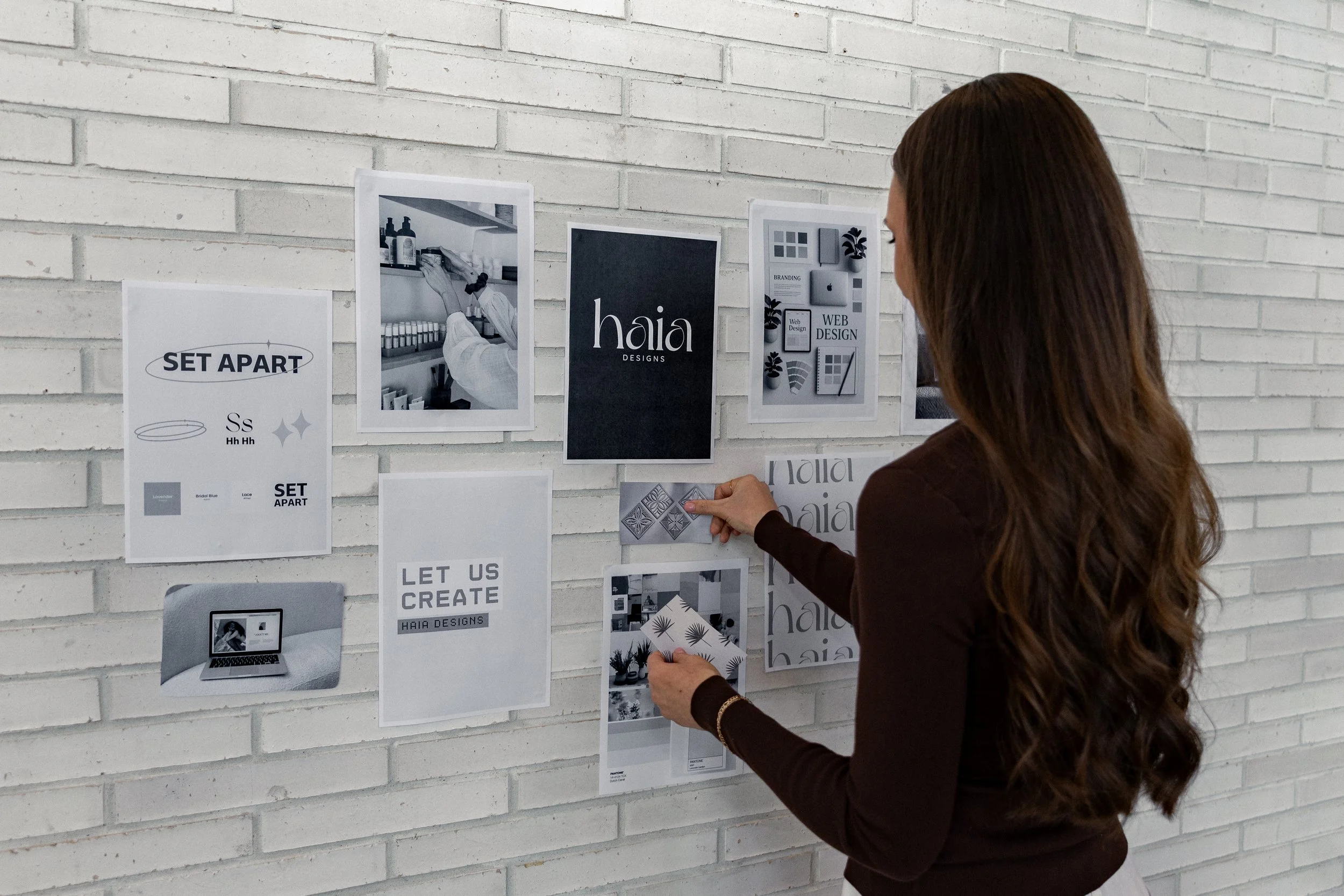 Woman looking at a white brick wall with various black and white printed images and posters related to design and branding.