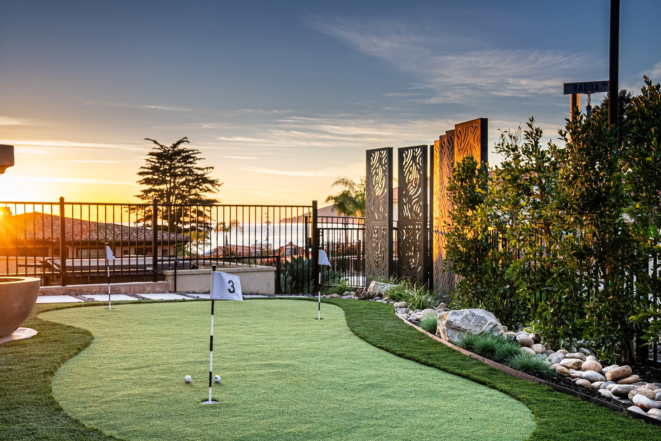 Miniature golf course with putting green, flags, and a decorative outdoor divider at sunset.