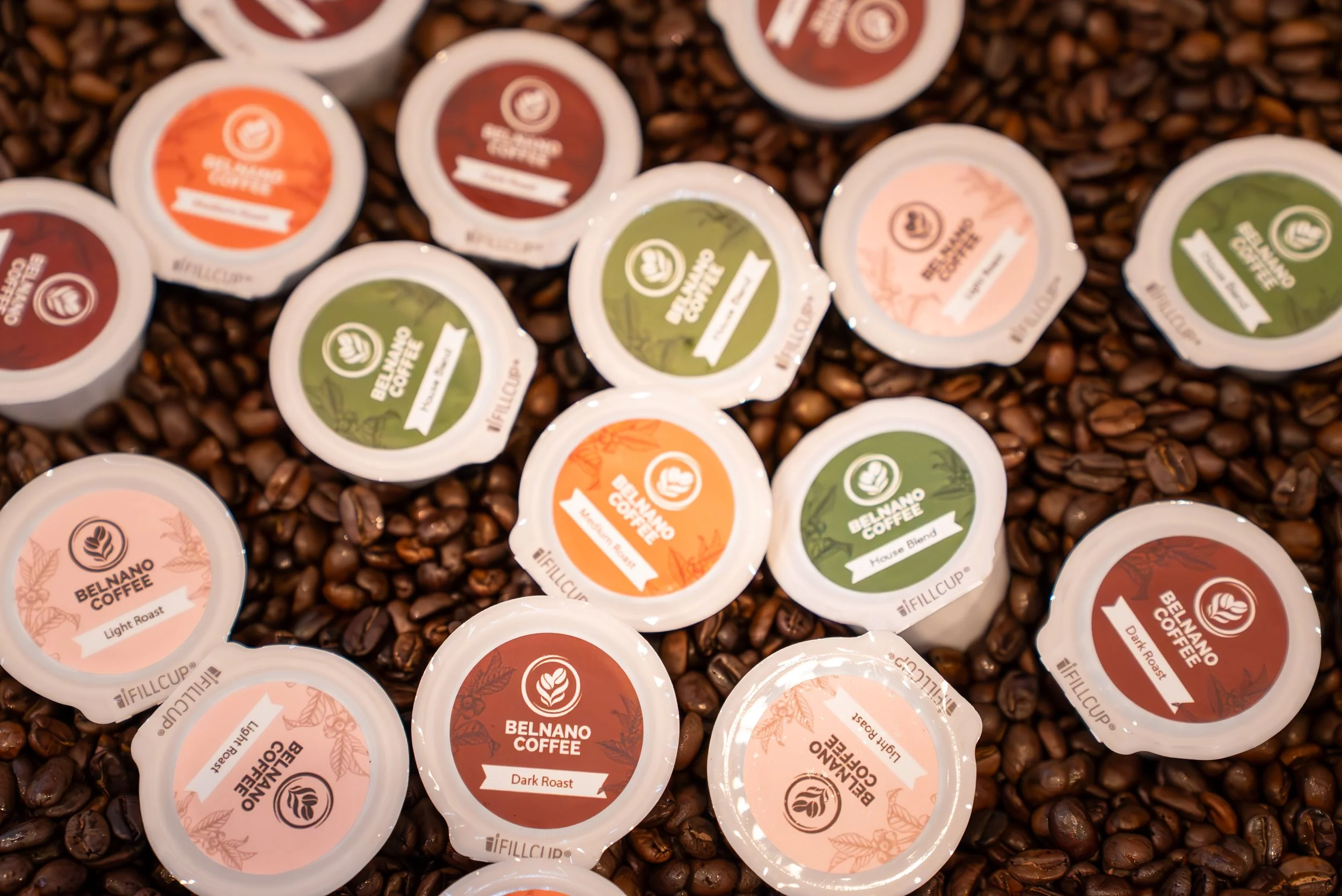 Assorted cups of BelNano Coffee flavor samples, featuring brand labels such as Light Roast, House Blend, Dark Roast, and others, spread on a bed of coffee beans.