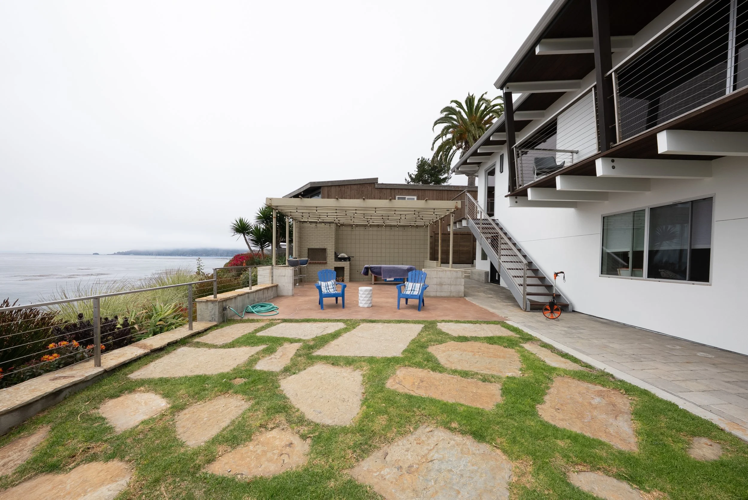 Backyard patio with blue chairs, palm trees, a barbecue grill, and ocean view.
