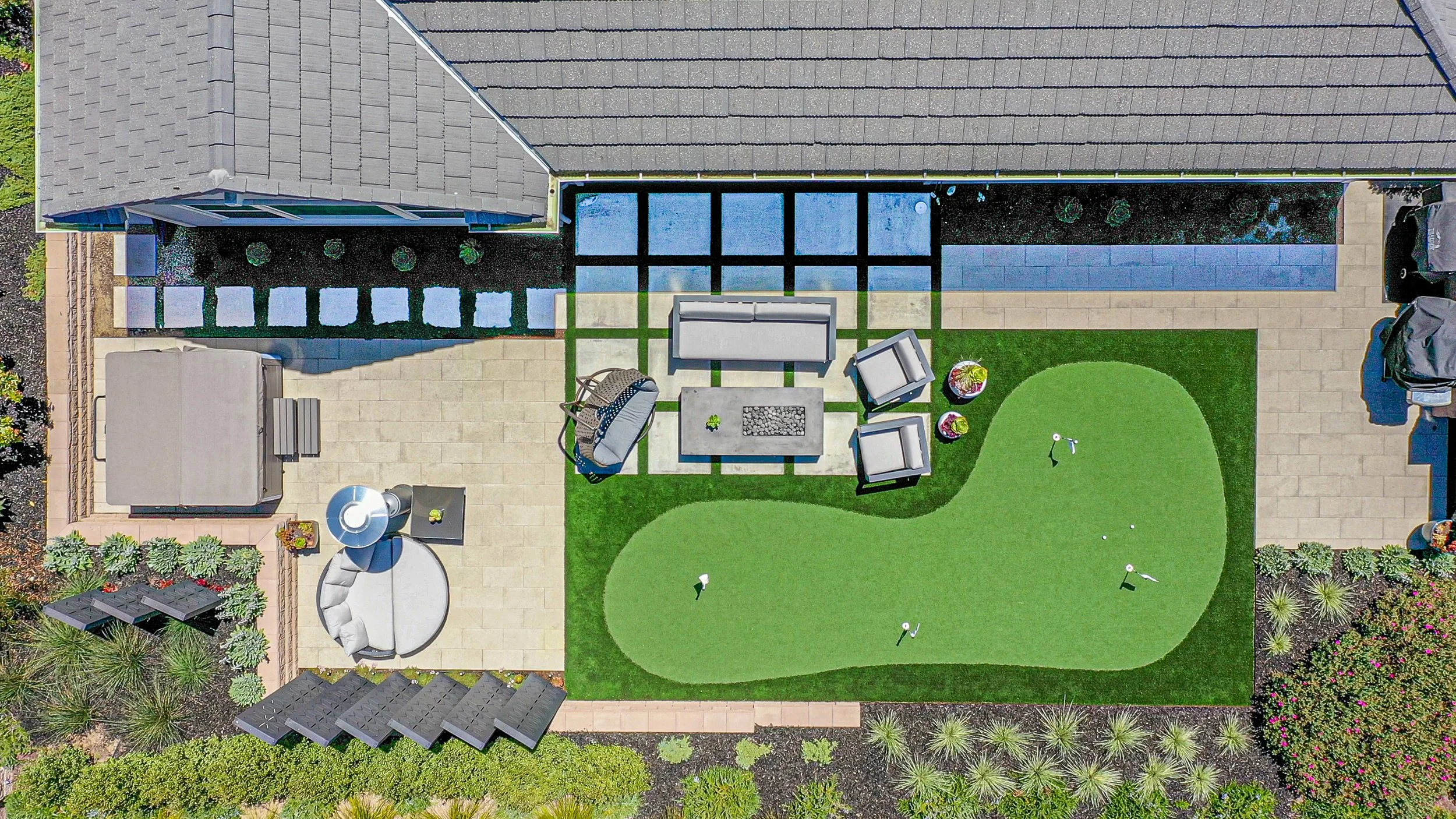 Aerial view of a backyard with a small putting green, patio furniture, a gazebo, and surrounding plants and landscaping.