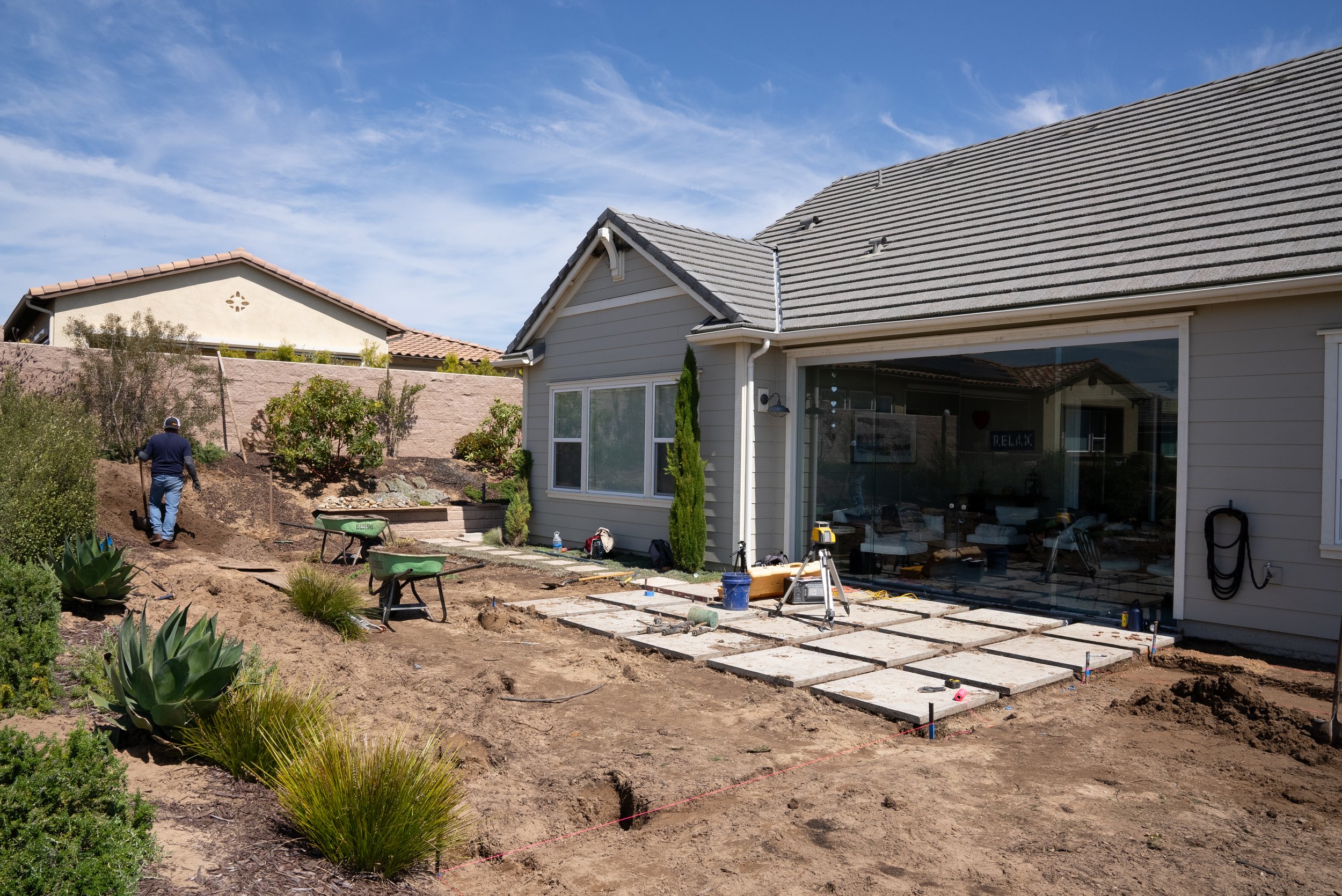 Residential backyard renovation in progress with paver stones, construction tools, and landscaping work.