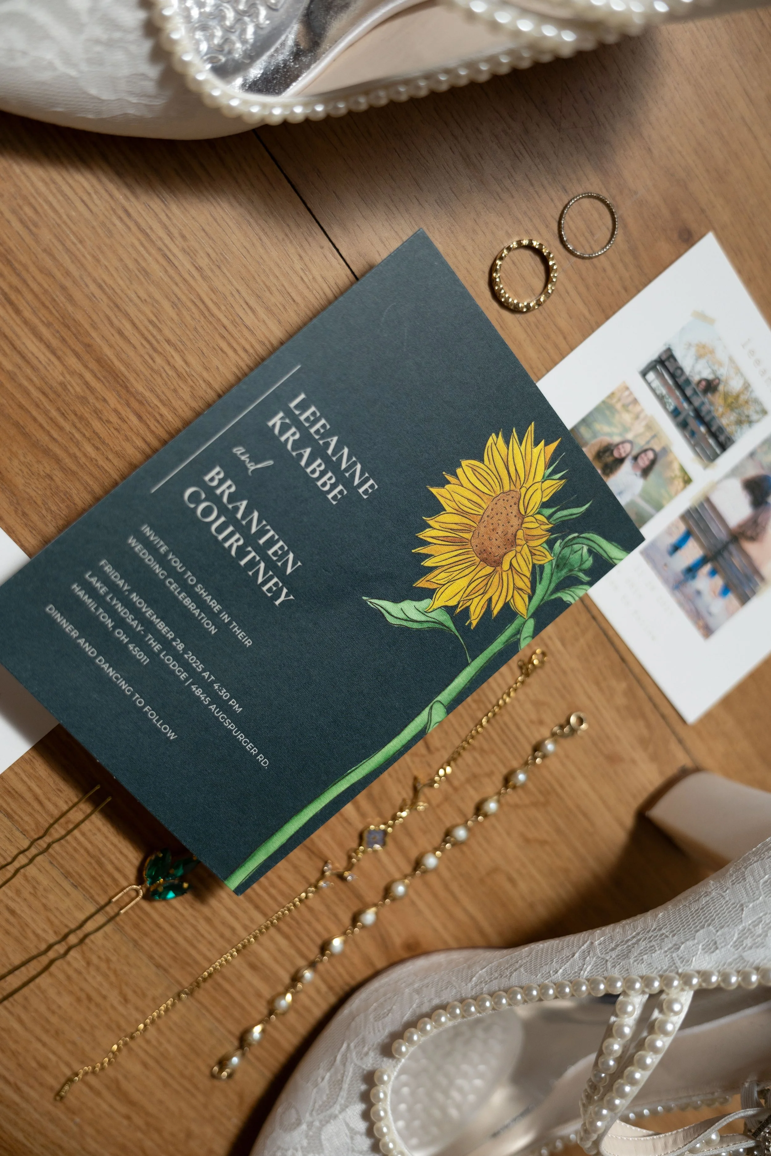 Wedding invitation card with sunflower illustration, jewelry, and a photo strip on a wooden table.