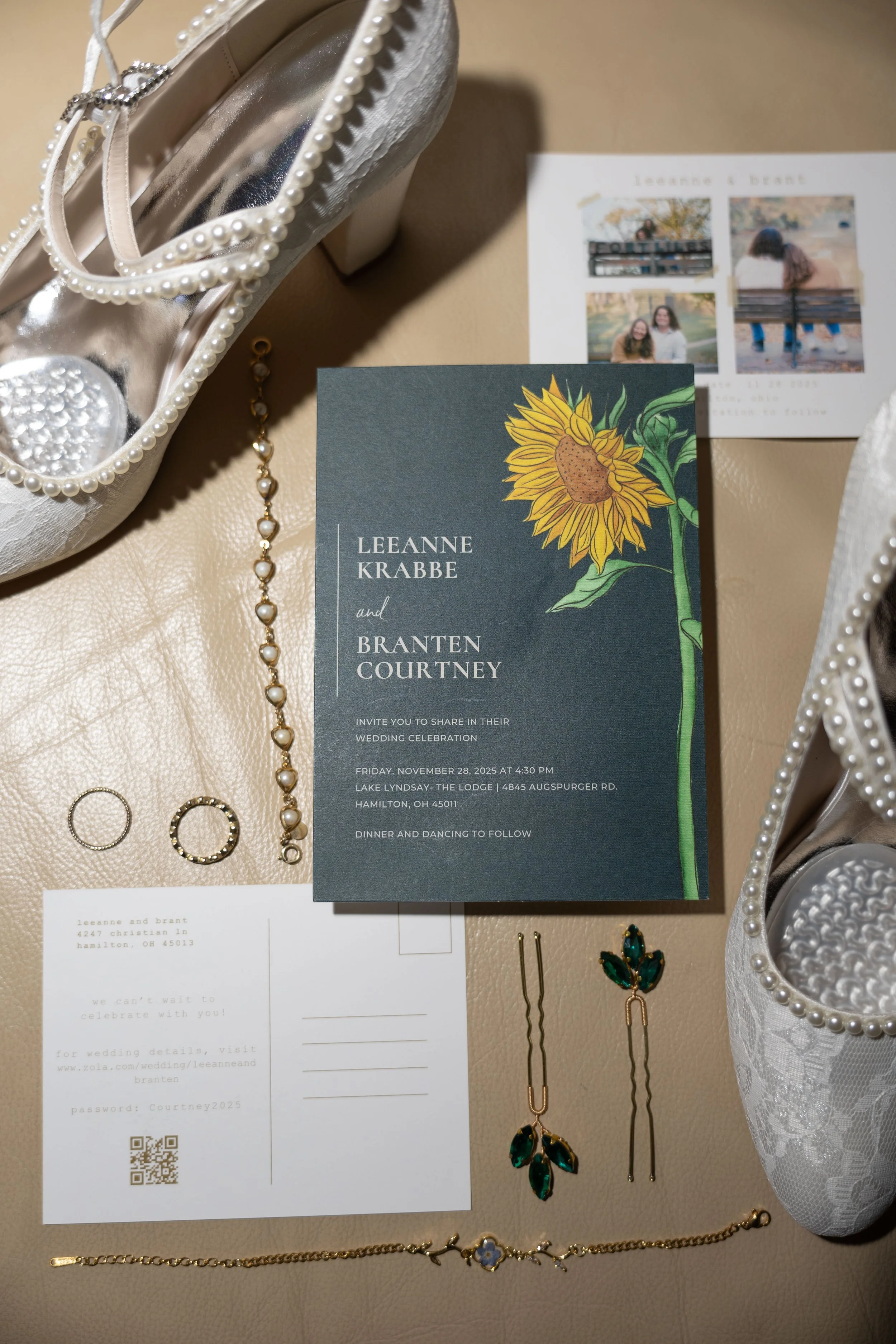 Wedding invitation card with sunflower illustration, rings, earrings, a bracelet, a pair of shoes decorated with pearls and lace, and a small printed photo of two women sitting on a bench in a park.